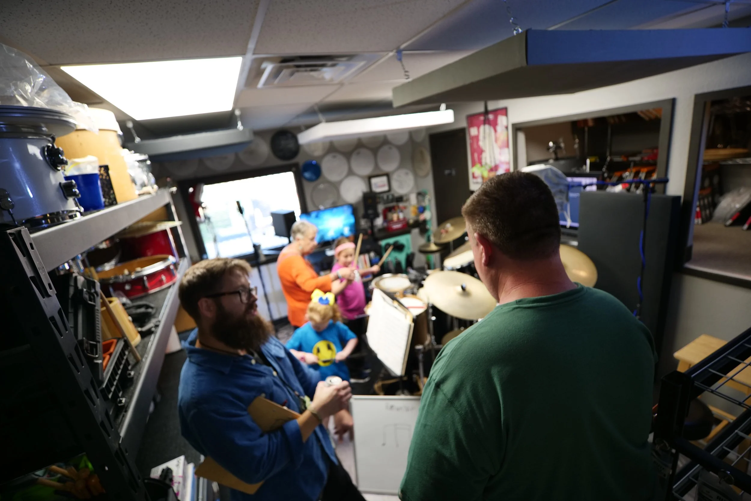 People playing drums and children in a music studio or rehearsal space.