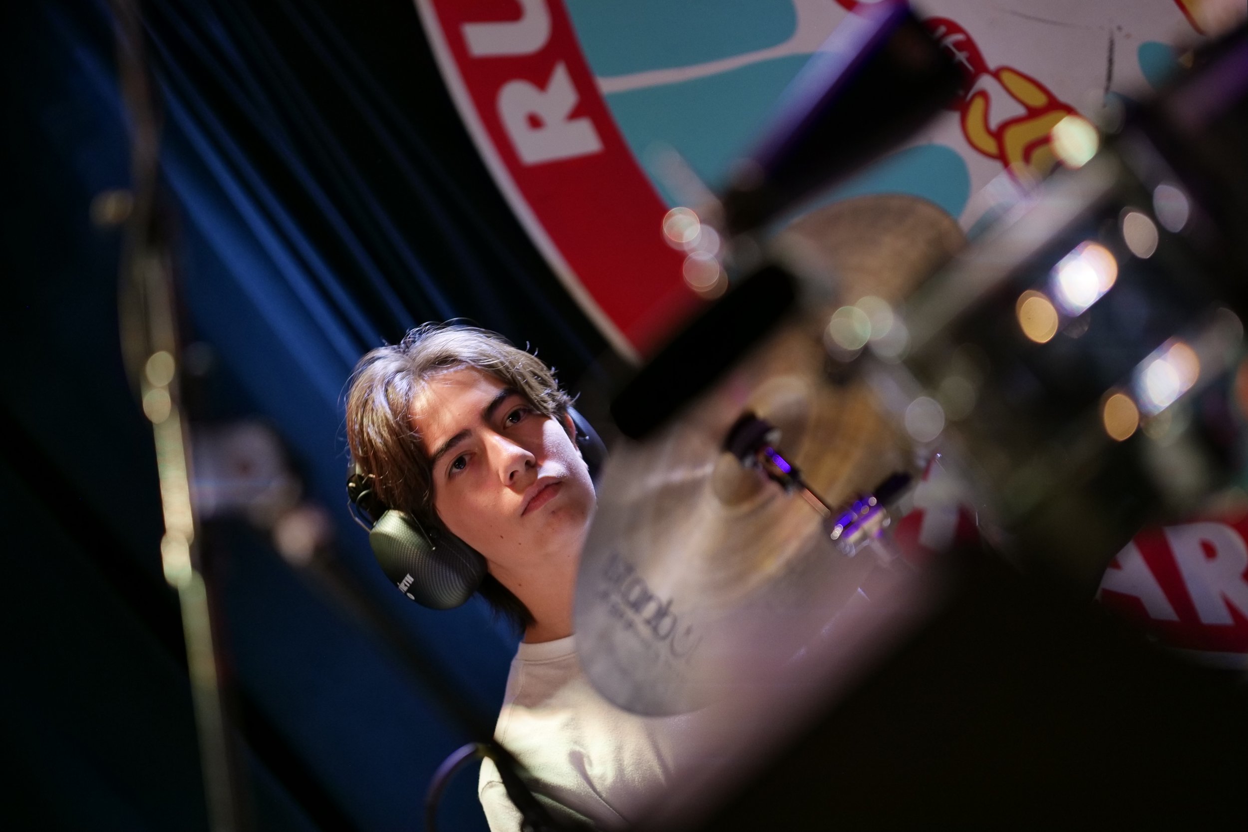 Young man with headphones looking at a coffee cup on a table, with a blurred colorful arcade game in the background.