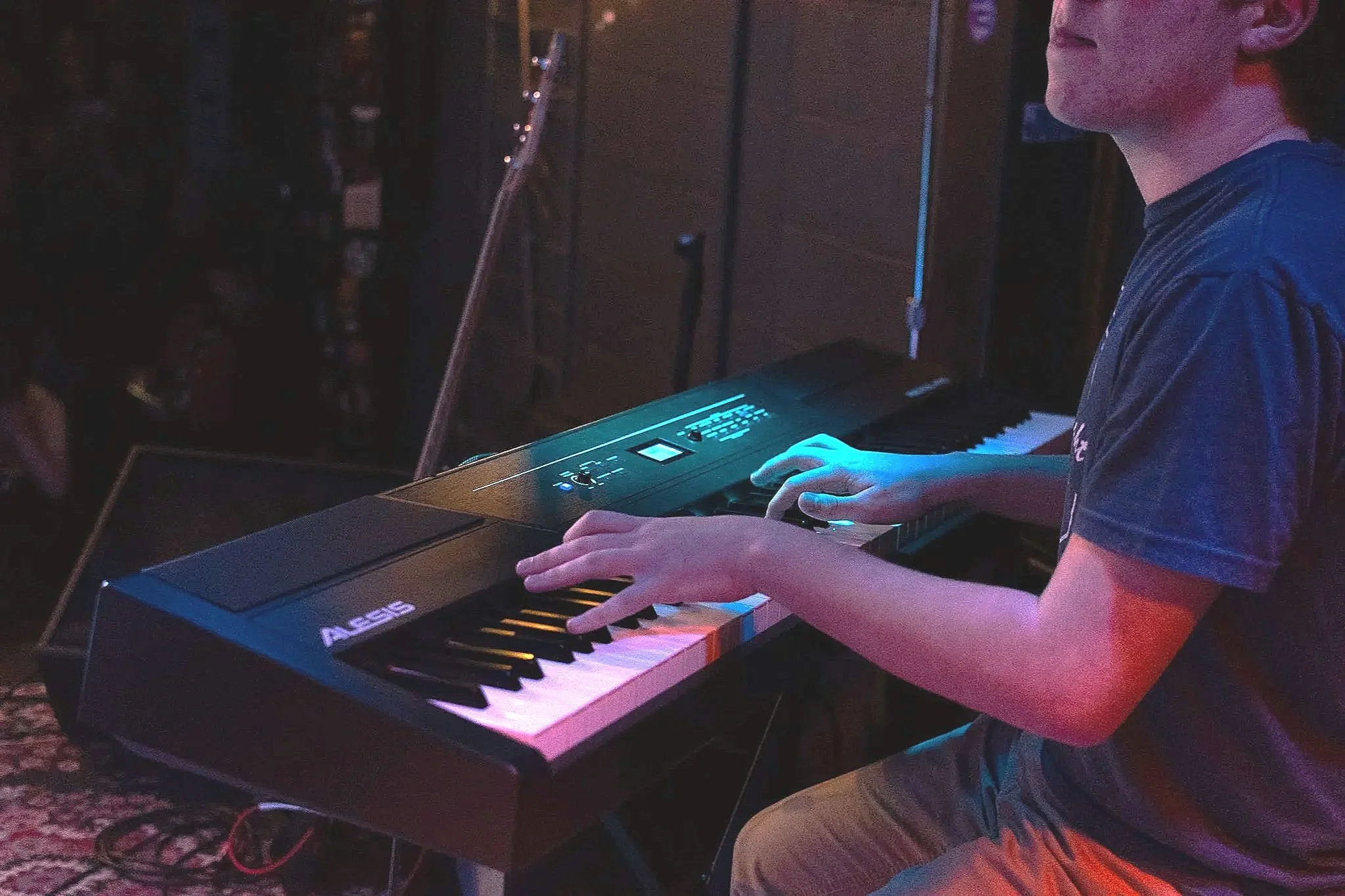 Person playing a digital keyboard on stage with colorful lighting.