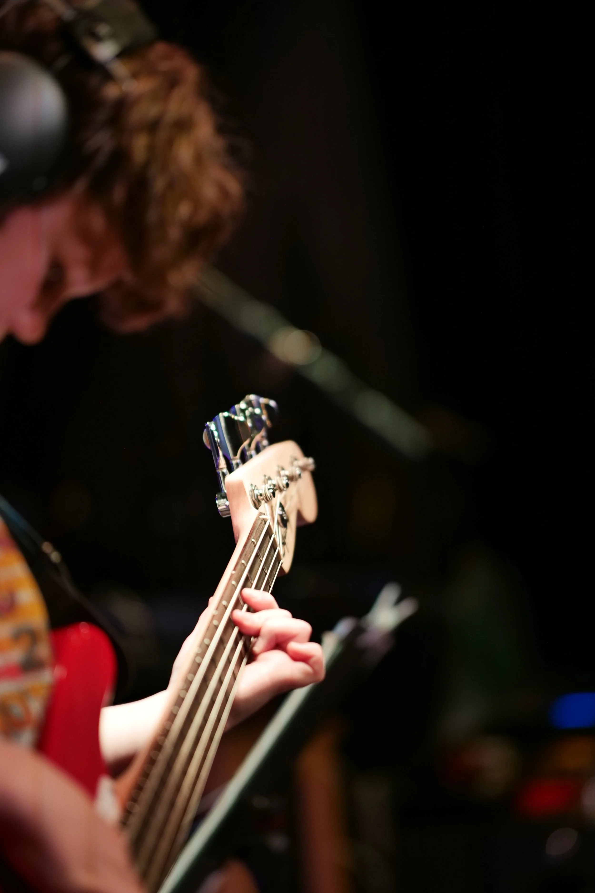 Person playing an electric bass guitar with sheet music and headphones in a recording studio.