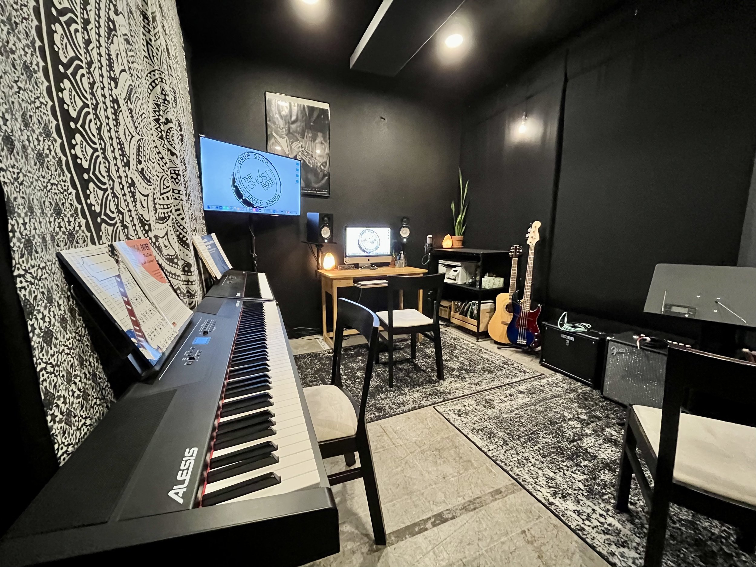 Music studio with a digital piano, guitars, studio monitors, and a computer setup, with dark walls, patterned curtains, and a patterned rug.