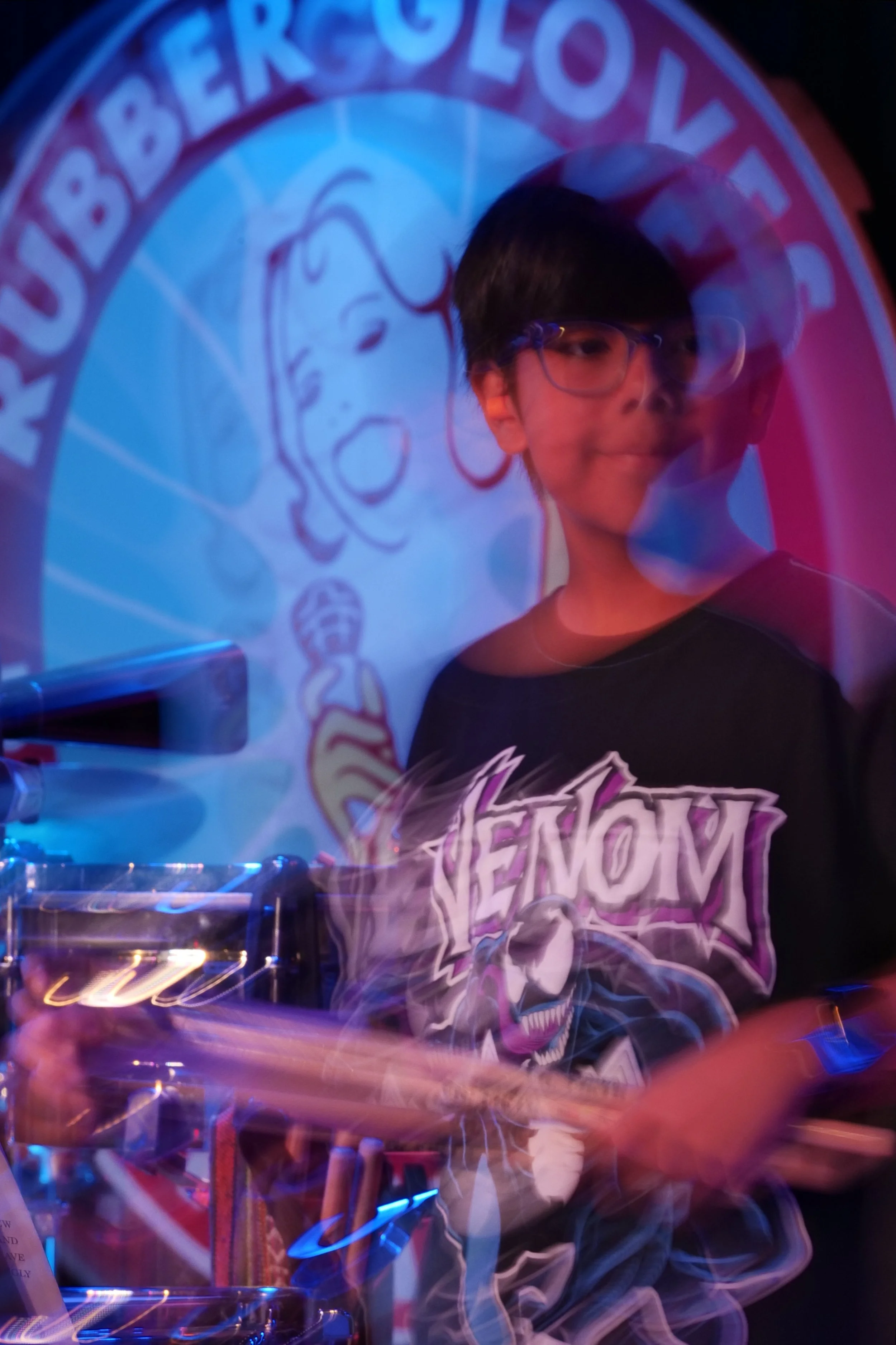 A boy with glasses standing in front of a projected logo of the Arkansas Geek Society, wearing a black T-shirt with a venom graphic on it, and holding a tablet.