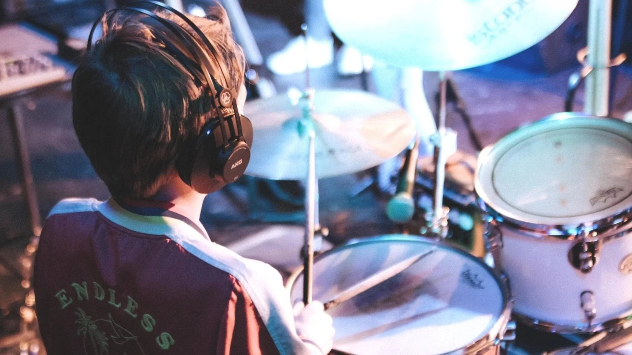 A person wearing headphones playing a drum set on stage during a performance.