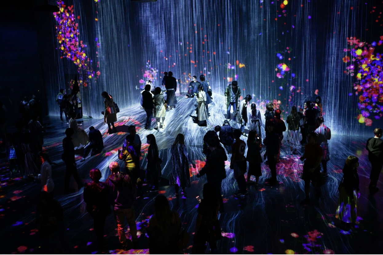 People walking inside a large immersive digital art installation with projected visuals on walls.