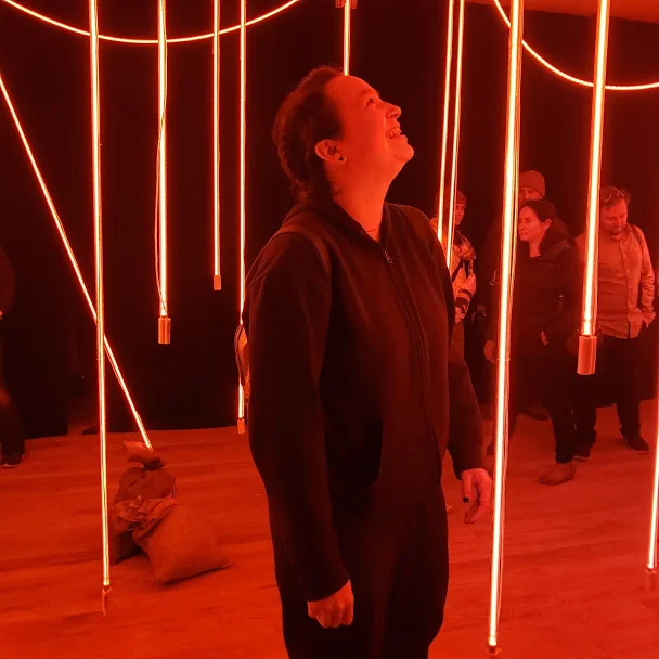 The author’s friend looking closely at the main exhibit, where strings of neon lights hang from the ceiling and surround viewers in red light. Photo Credit: Alyssa Wroblewski