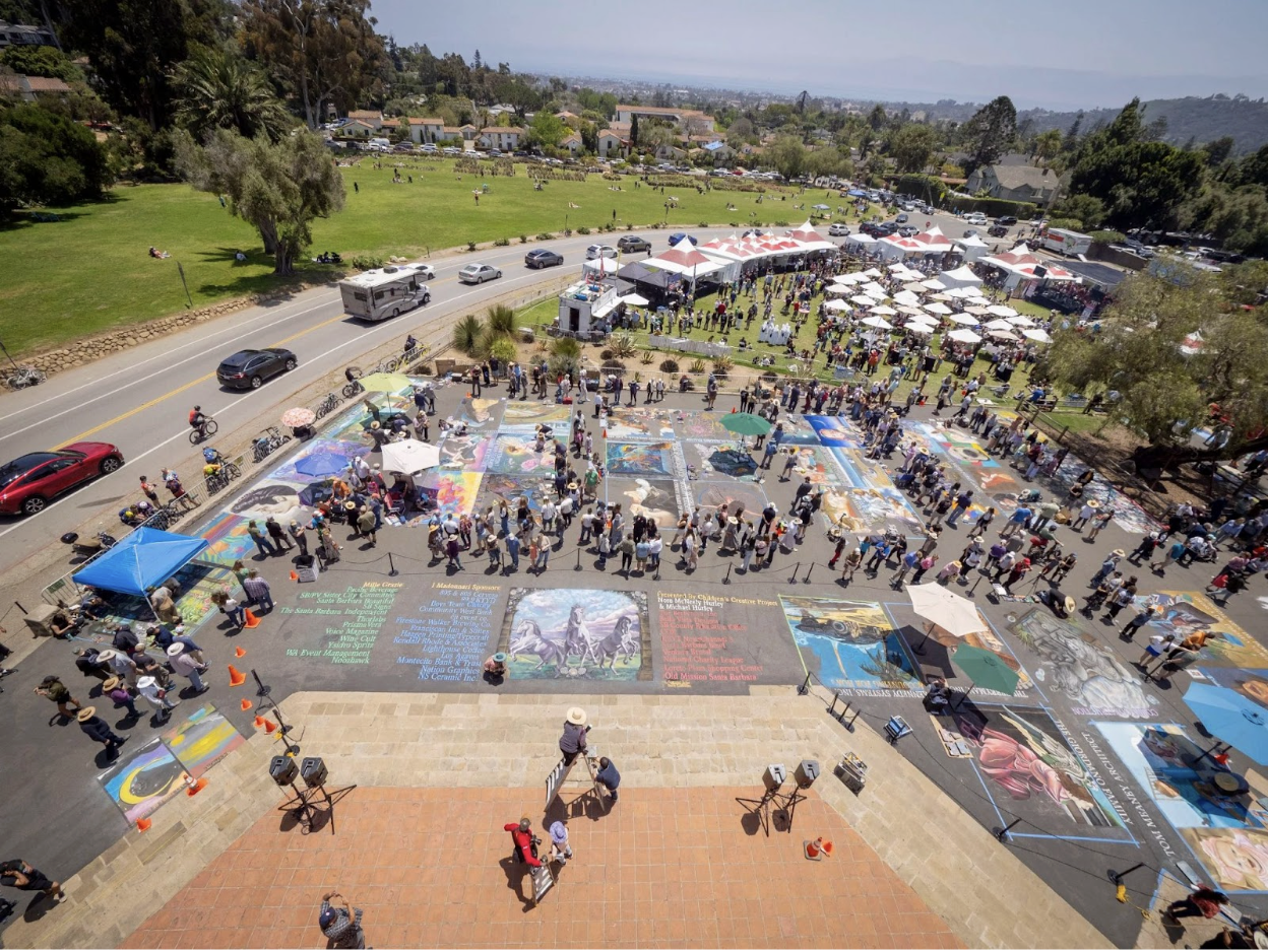 Street artists creating large-scale chalk drawings on pavement during the I Madonnari Festival.