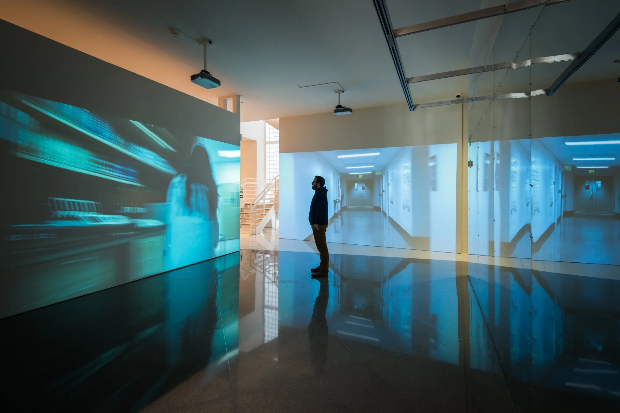 A room-sized screen installation, with one person standing in the middle. The screens show images of hallways and moving figures.