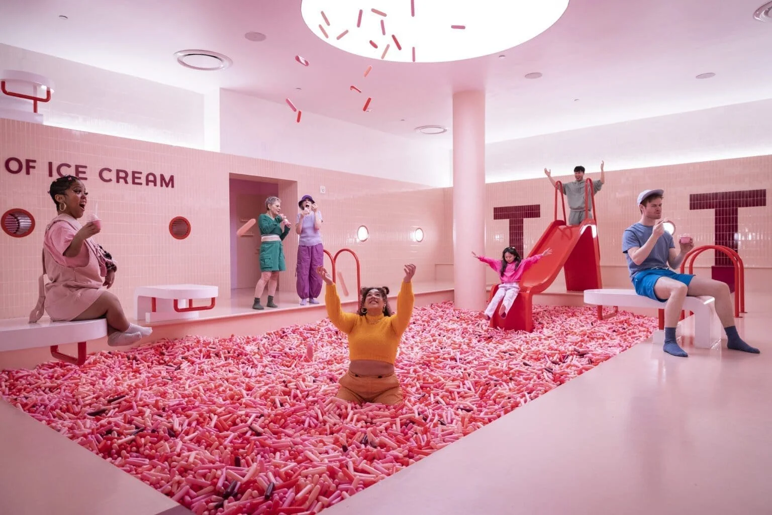 A group of people play and interact with a pink pool full of sprinkles at the Museum of Ice Cream.