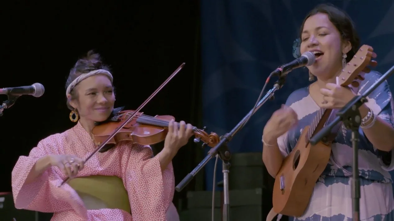 Two women performing. One is playing the violin and the other is singing and playing guitar.