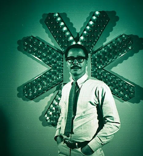 Photo of  a man standing in front of light sculpture shaped like a star, with green tint on photo.