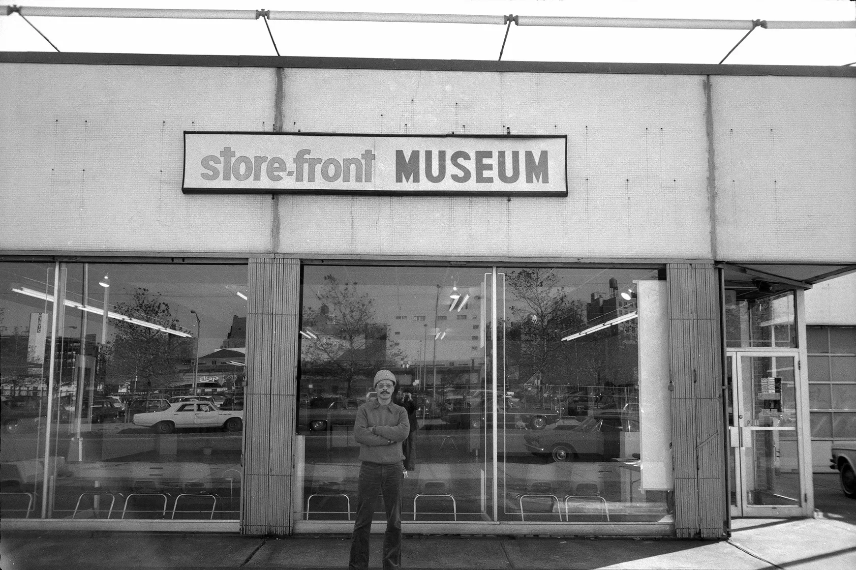 Black and white photo of a man standing in front a building with the name "Store Front Museum."