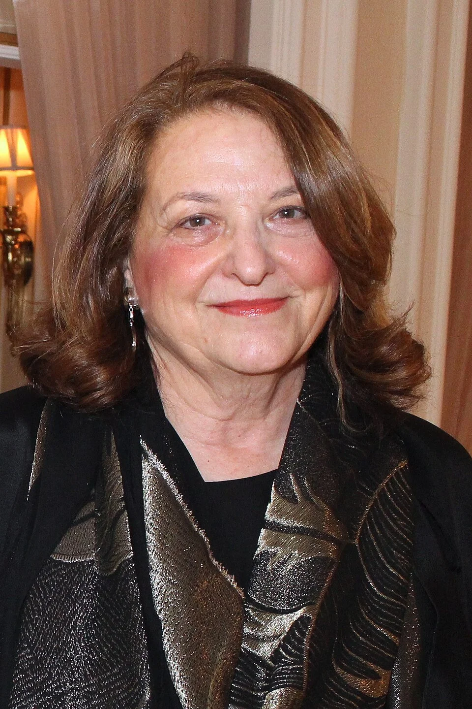 Portrait of woman smiling with auburn hair, red lipstick, and black and sliver blouse.