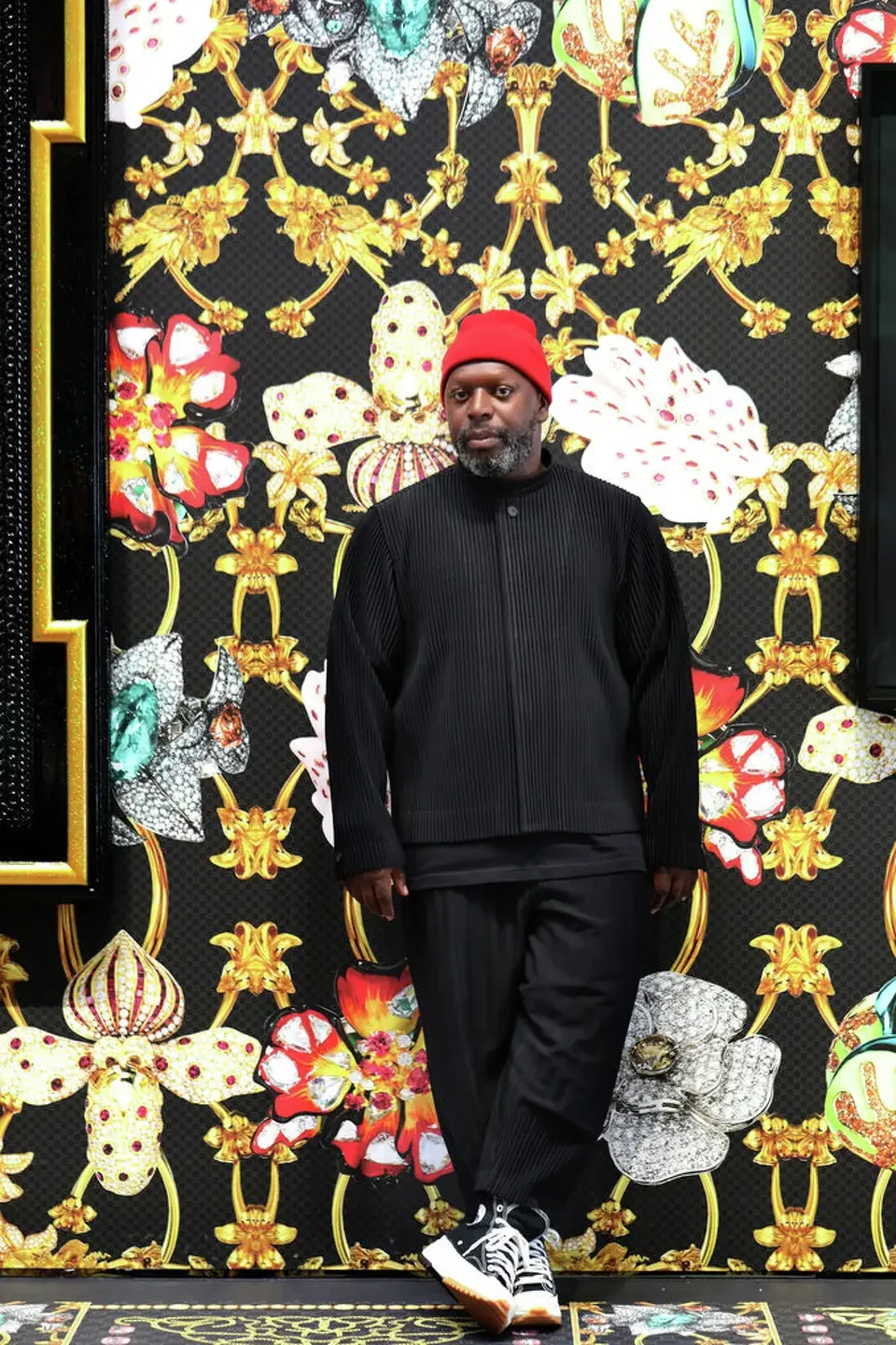 Man in a red hat and black outfit standing in front of a floral background.