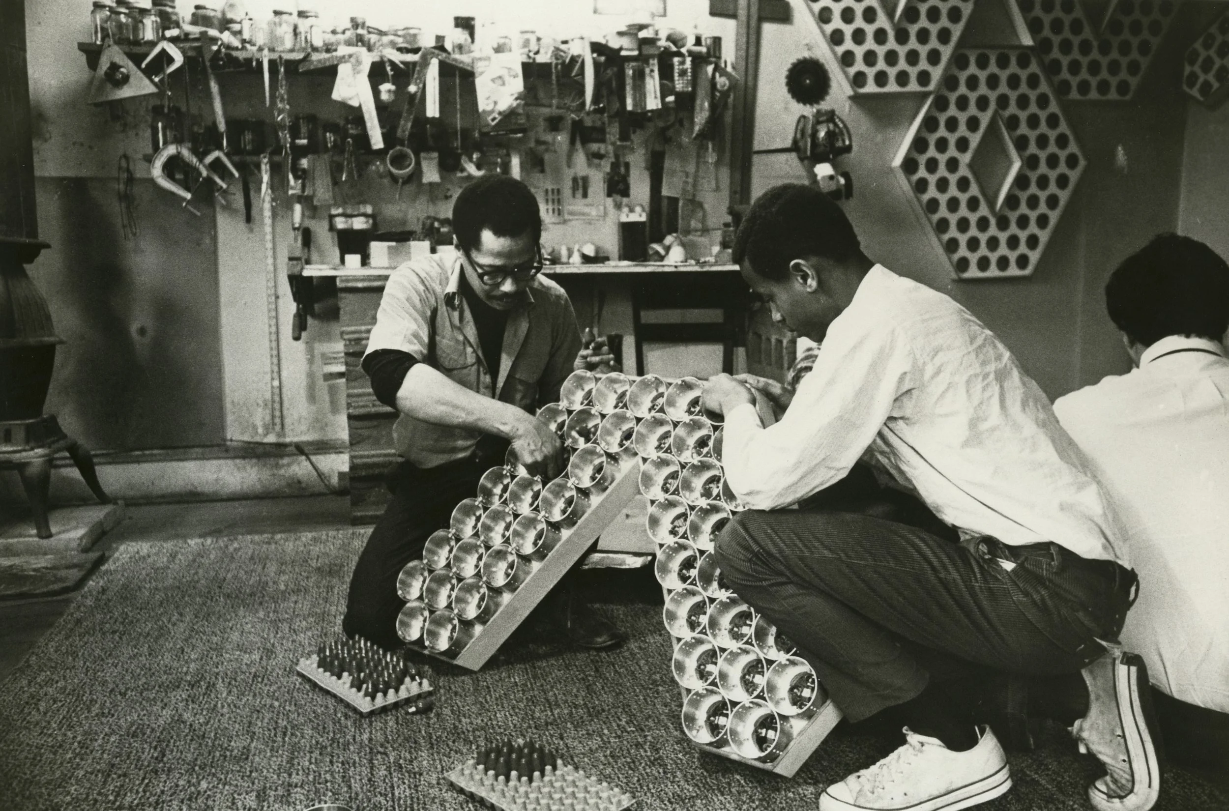 Black and white photo of two men working on mechanics of a light sculpture
