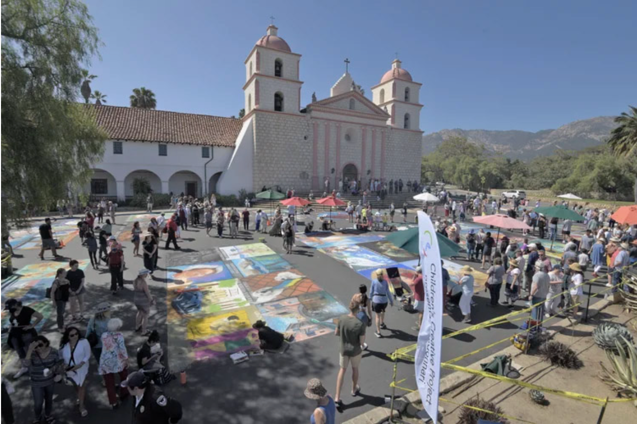 Large crowd gathered around chalk artworks at an outdoor street art festival.