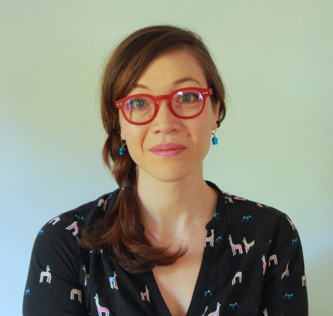 Portrait of woman with red glasses, a braid to the side, and llama printed blouse.