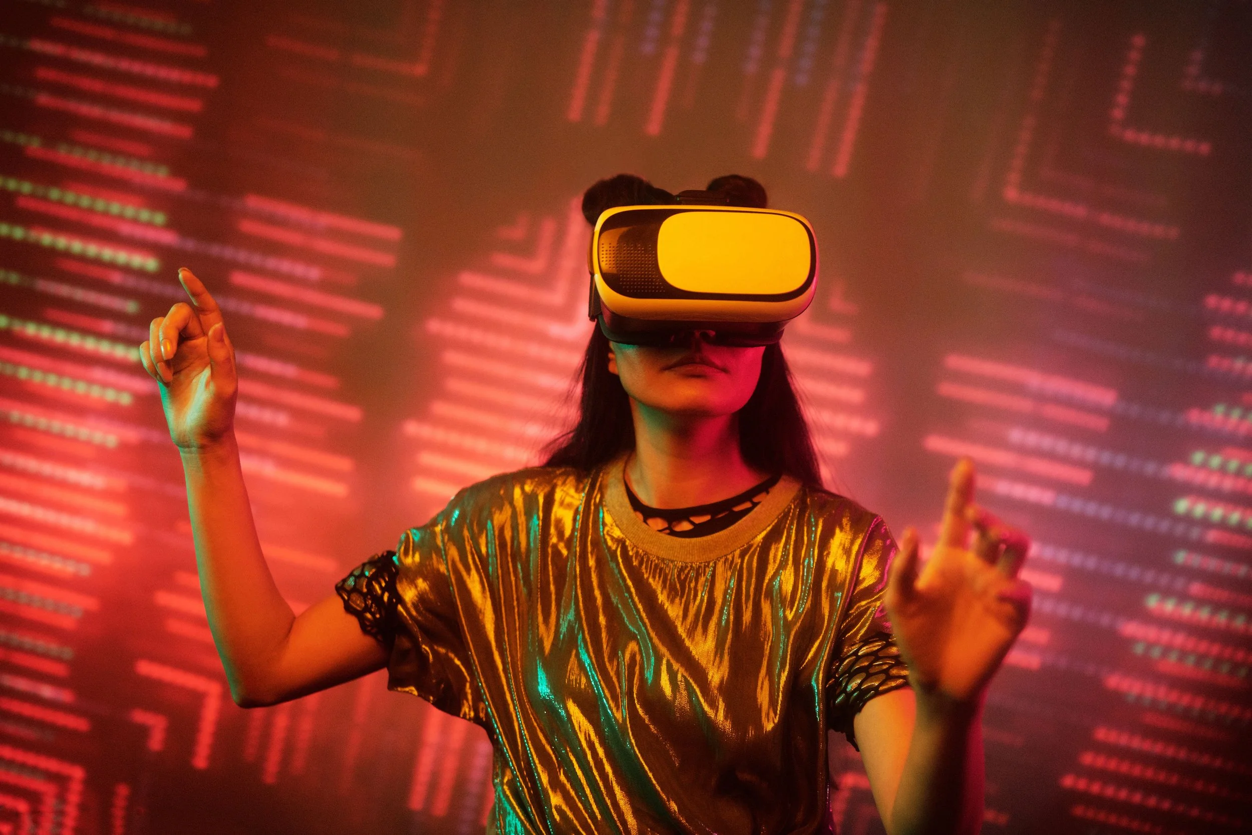 A woman, who is wearing a metallic top, uses a virtual reality headset immersed in a digital environment with vibrant orange and red lights.