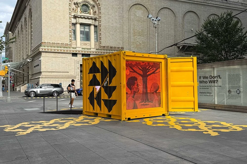 Yellow storage crate, sitting on the edge of a Brooklyn street corner, embedded with a reddish digital screen image of two Black people.