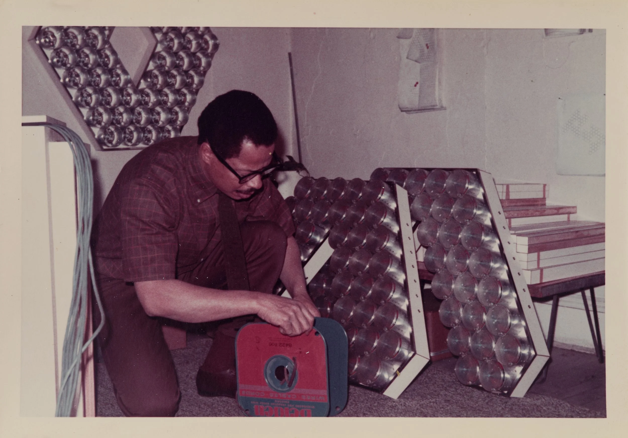 Man knelt down working on mechanical sculpture with large light fixture.