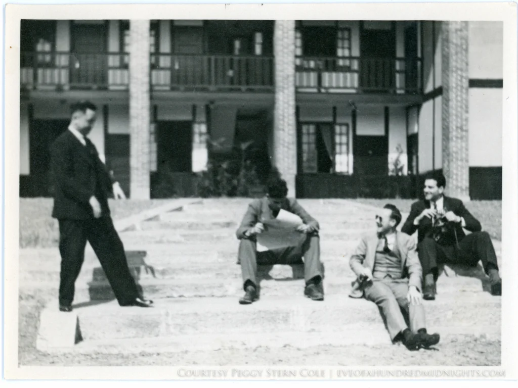 Hugh Deane Reading Paper as Mel and other reporters goof around outside press hostel.jpg
