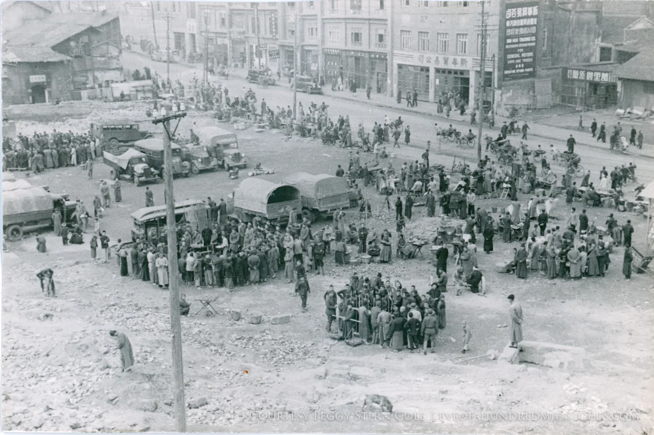 Crowds gathering by trucks beneath hill.jpg