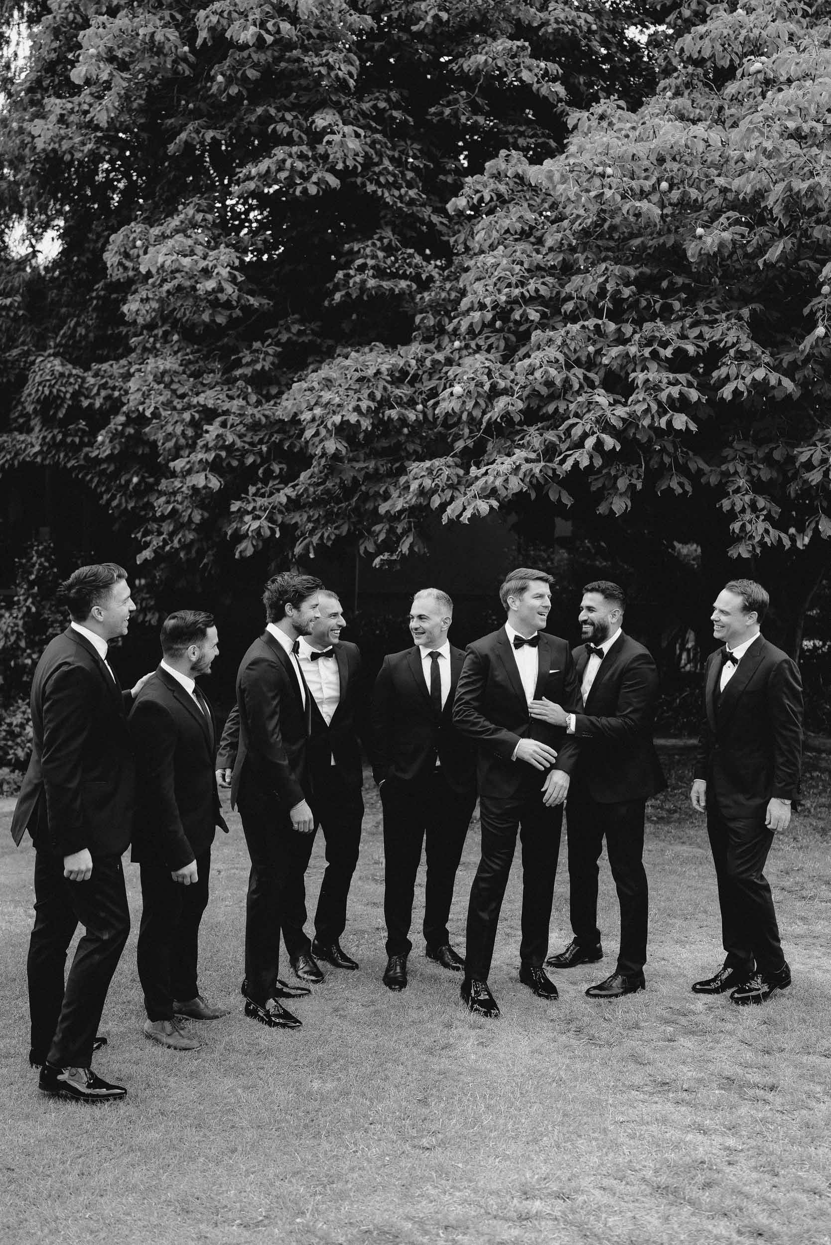 Groomsmen in black tie outfits gather and converse on wedding day