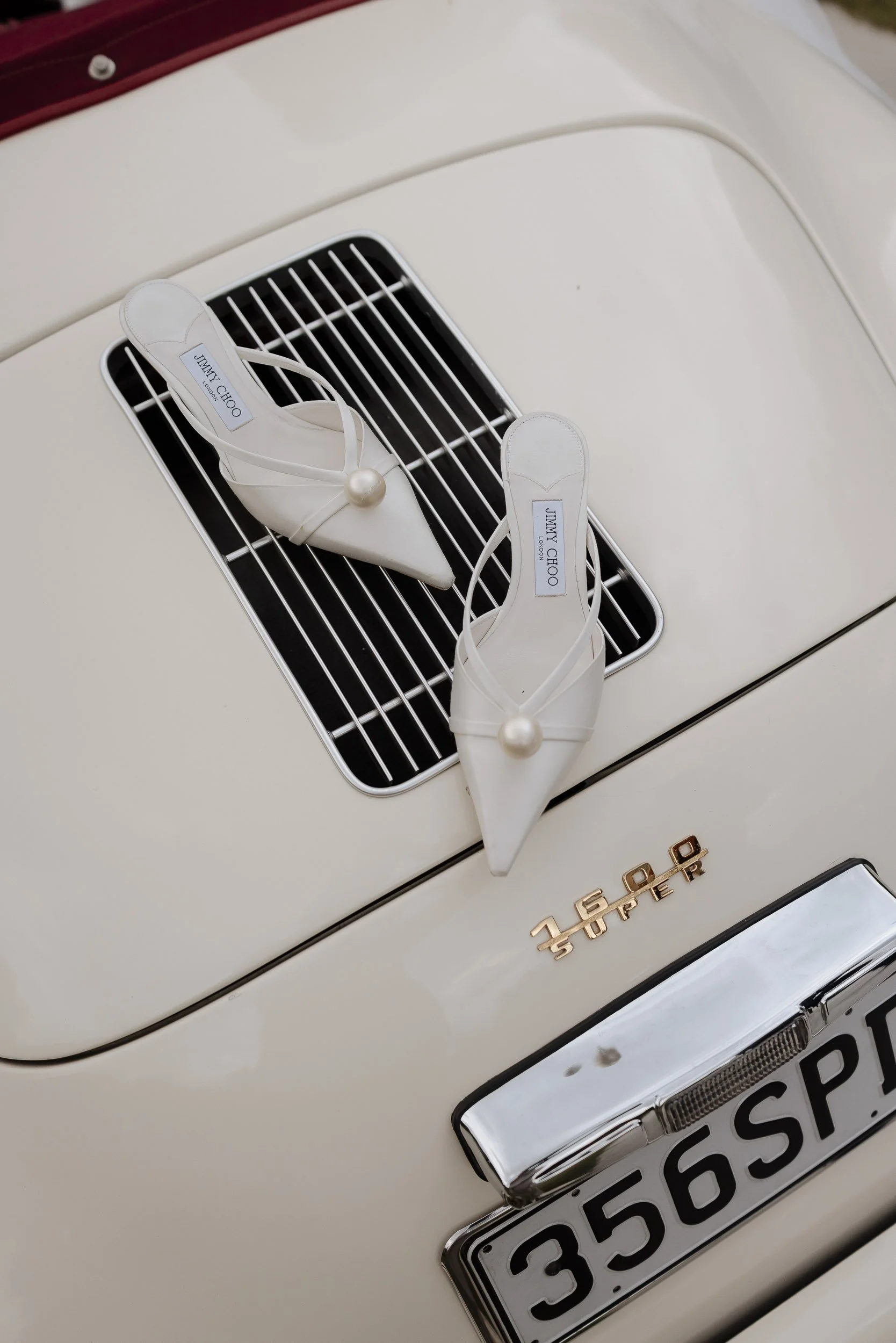 Jimmy Choo shoes laid on the boot of a vintage cream and red porsche 356 speedster car