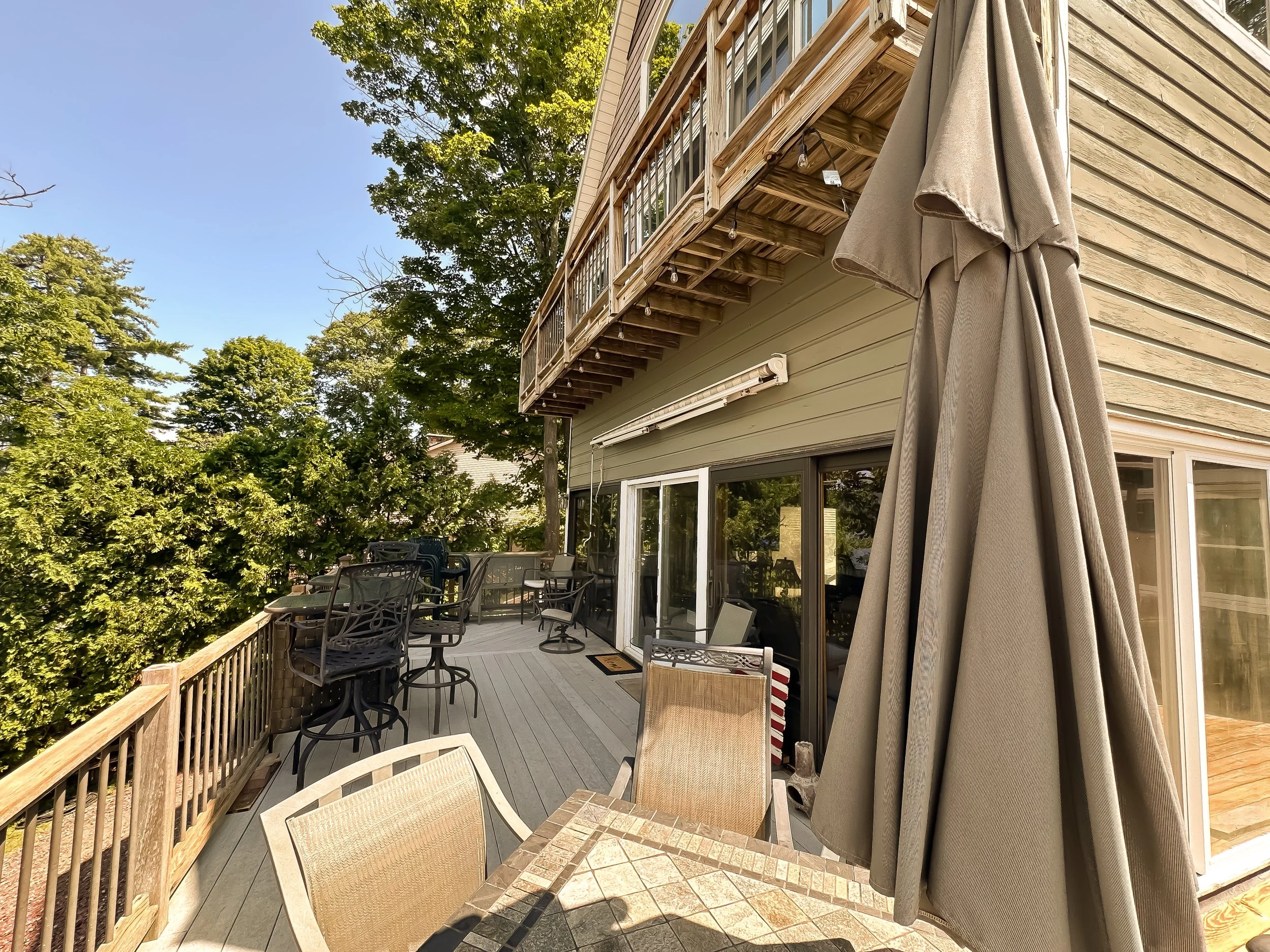 Backyard patio with outdoor furniture, plants, and trees, with a small balcony with string lights and a foldable umbrella.