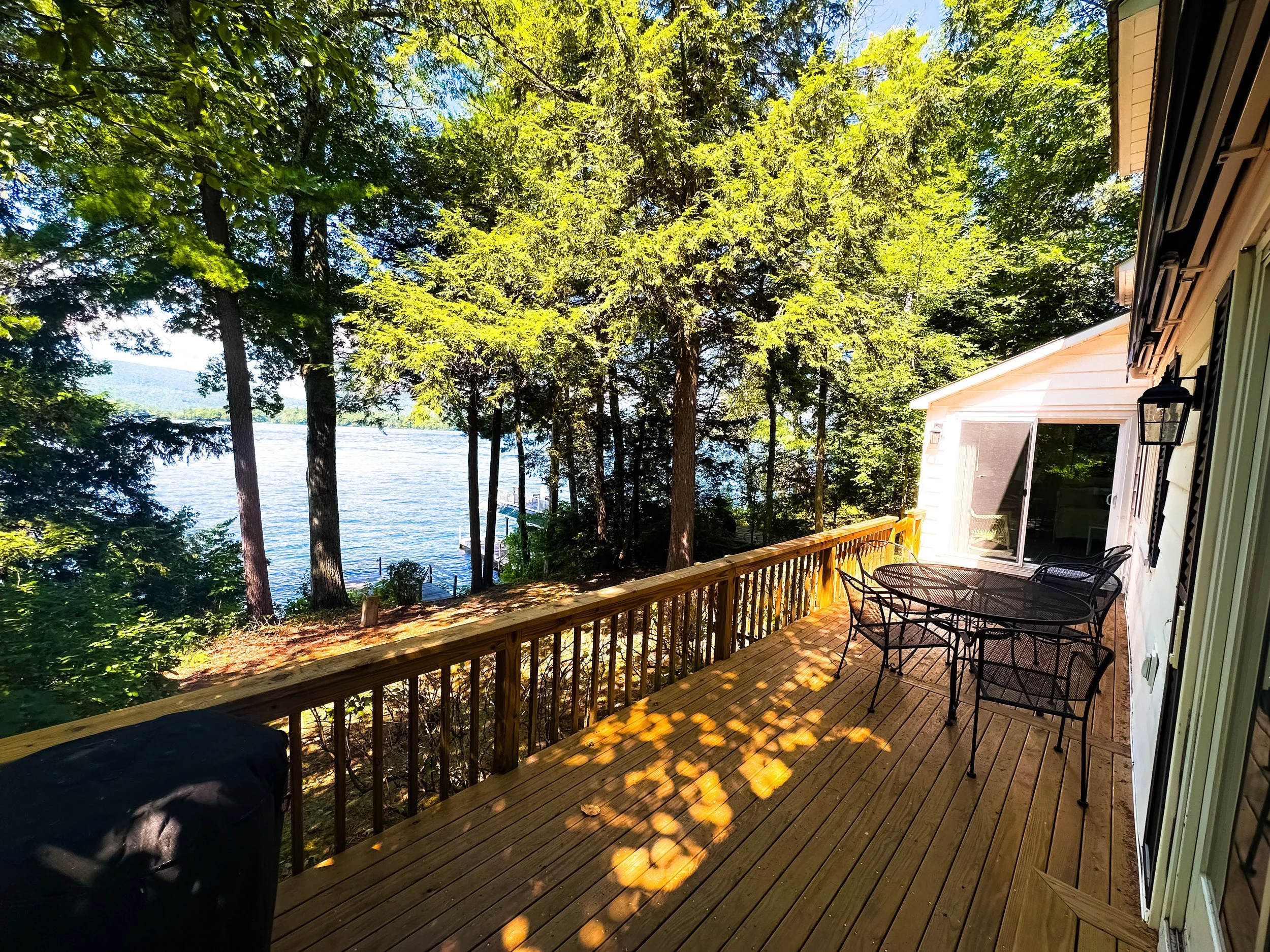 A wooden deck overlooking a lake with green trees and a house on the right side.