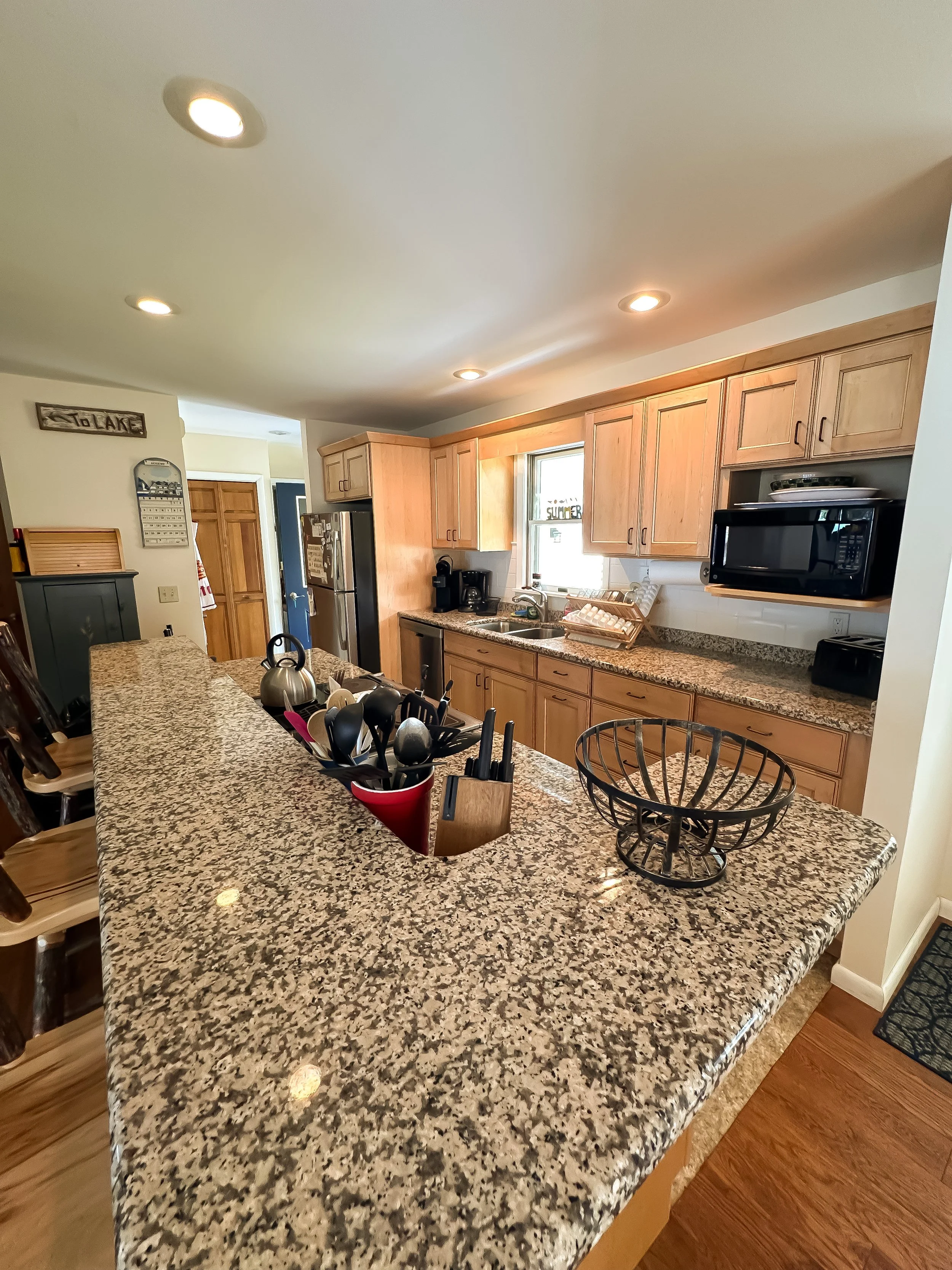 A spacious kitchen with a granite countertop island, wooden cabinets, a window above the sink, and various kitchen appliances including a microwave and coffee maker.