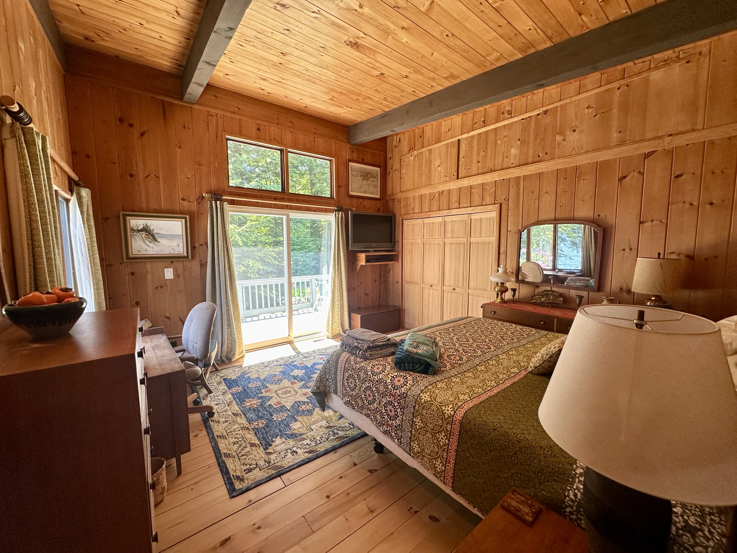 Wood-paneled bedroom with a bed, sliding glass door leading to a balcony, and a wall-mounted TV.