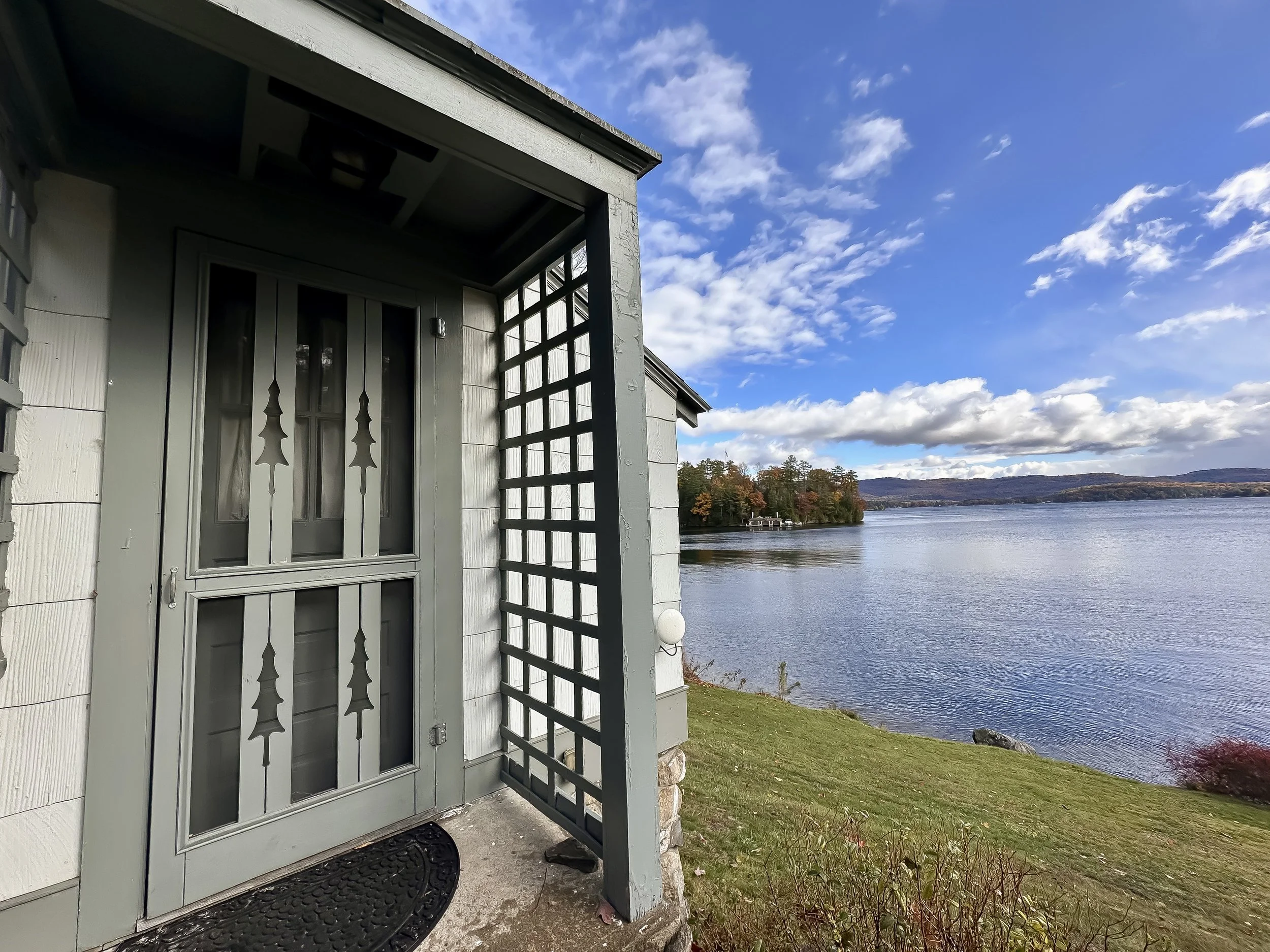View from a porch showing a lake with distant hills under a partly cloudy sky.