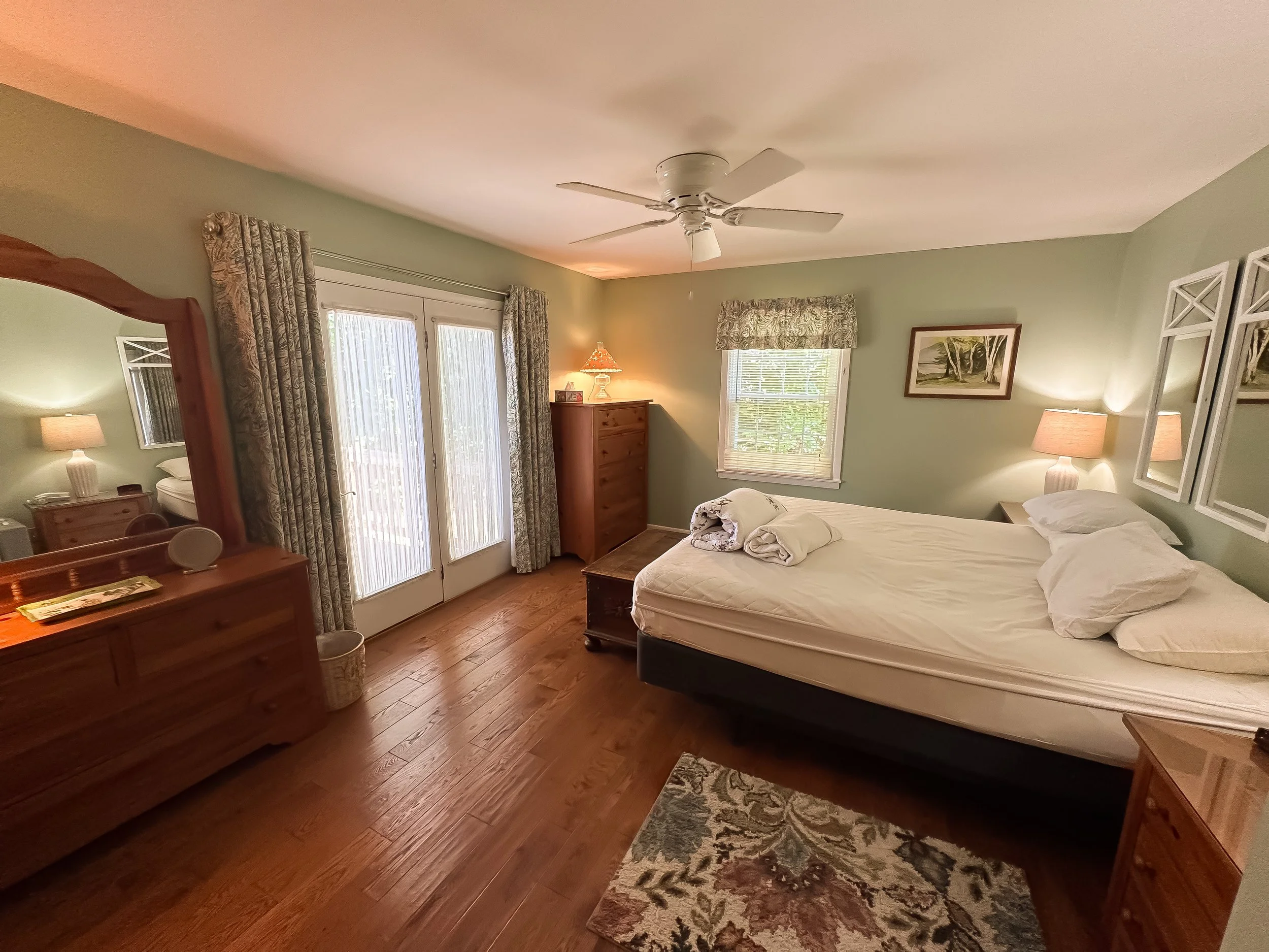 Bedroom with a bed, wooden furniture, a ceiling fan, and windows with curtains.