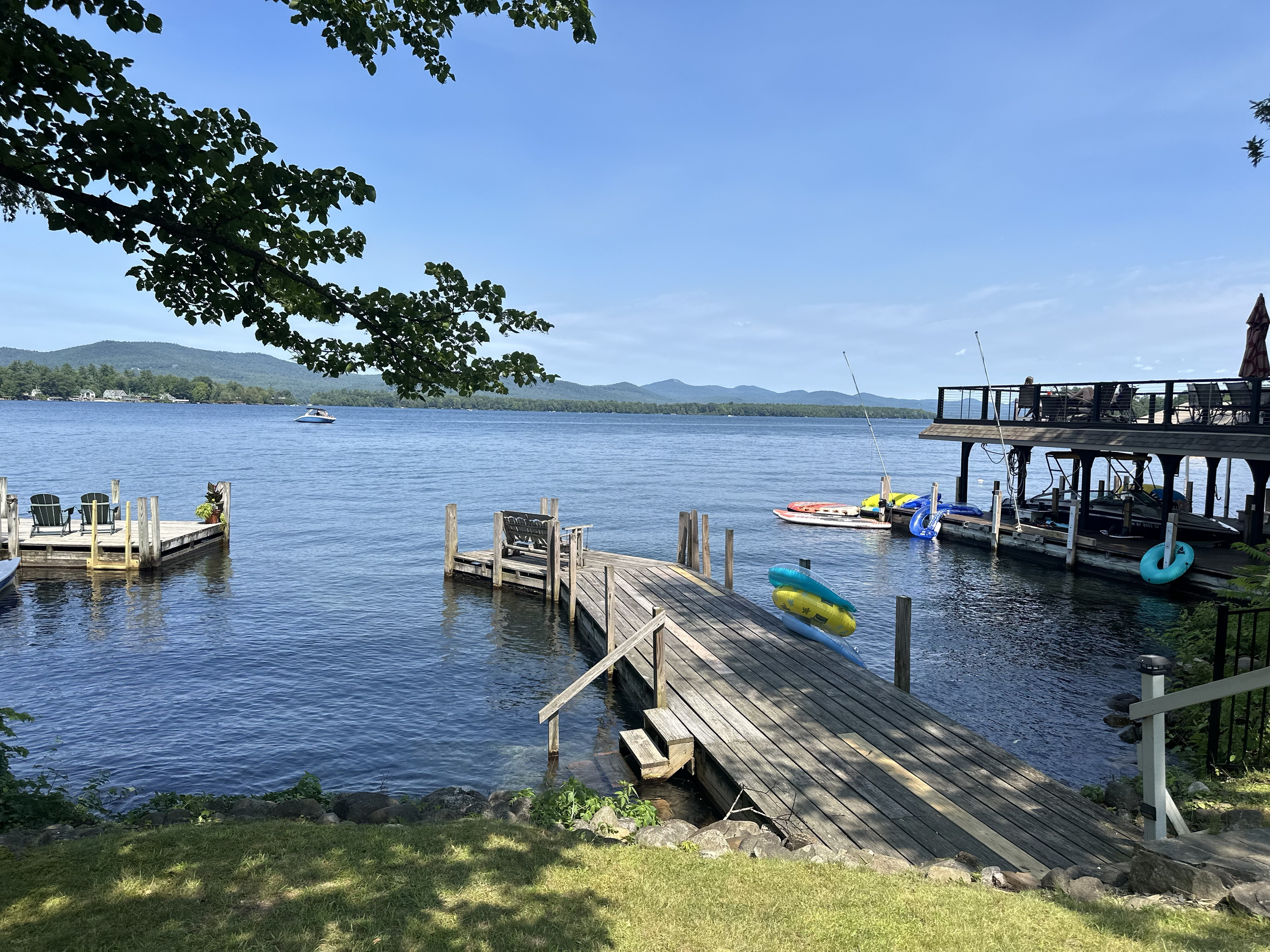 View of a lake with a dock and boats, surrounded by trees and mountains in the background.