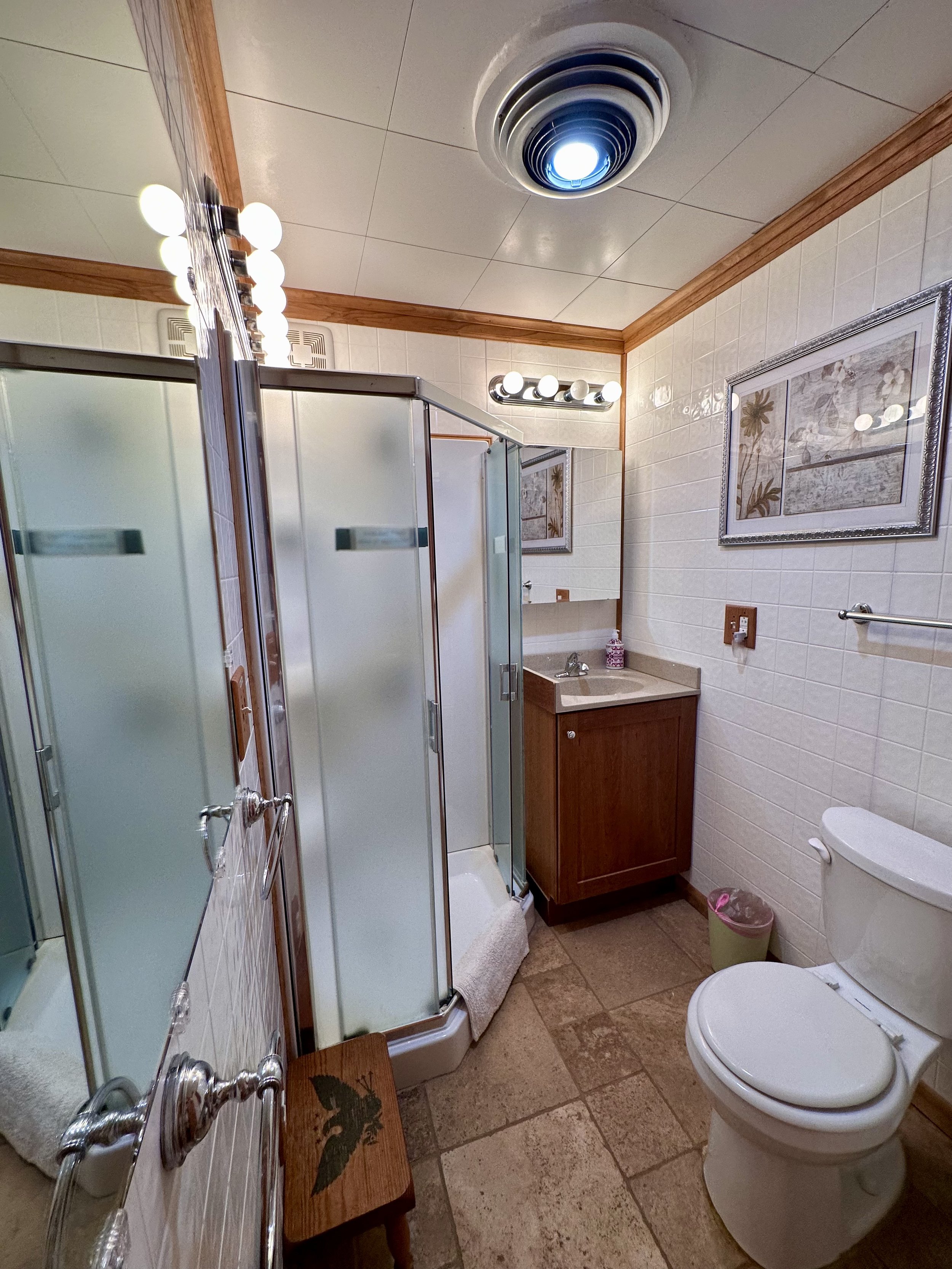 Small bathroom with a shower stall, toilet, wooden vanity with a sink, framed artwork, and a ceiling ventilation fan.
