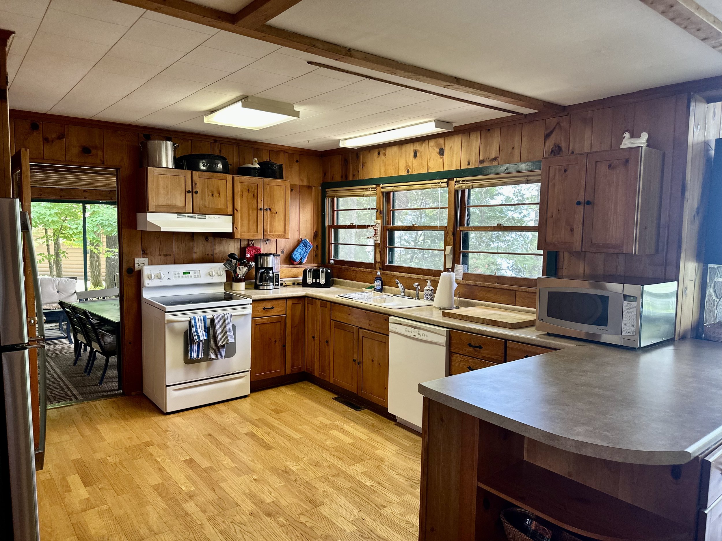 Wood-paneled kitchen with white stove, microwave, dishwasher, and large windows overlooking greenery