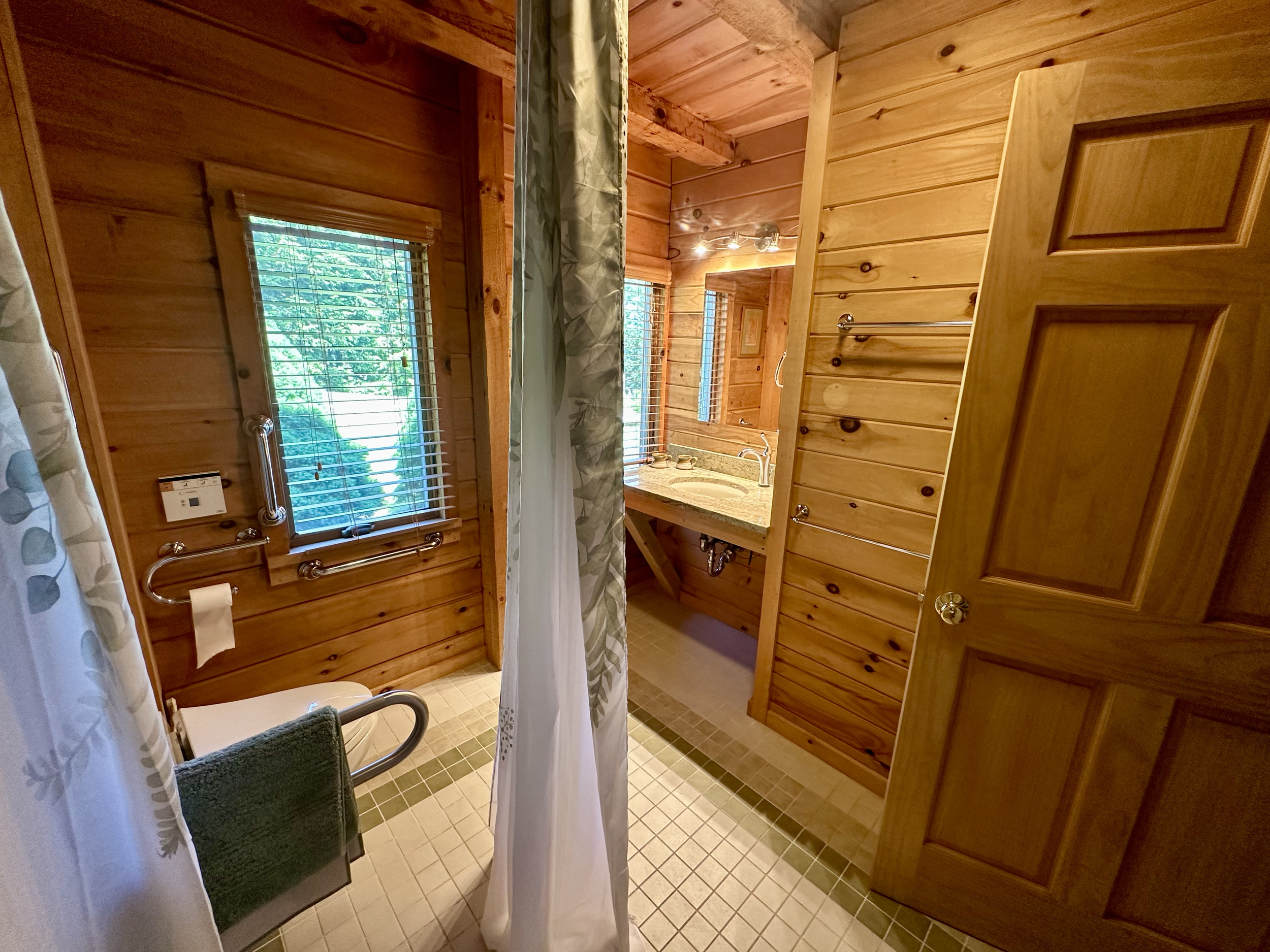 Wood-paneled bathroom with a window, shower curtain, sink with granite countertop, and a bathroom door.