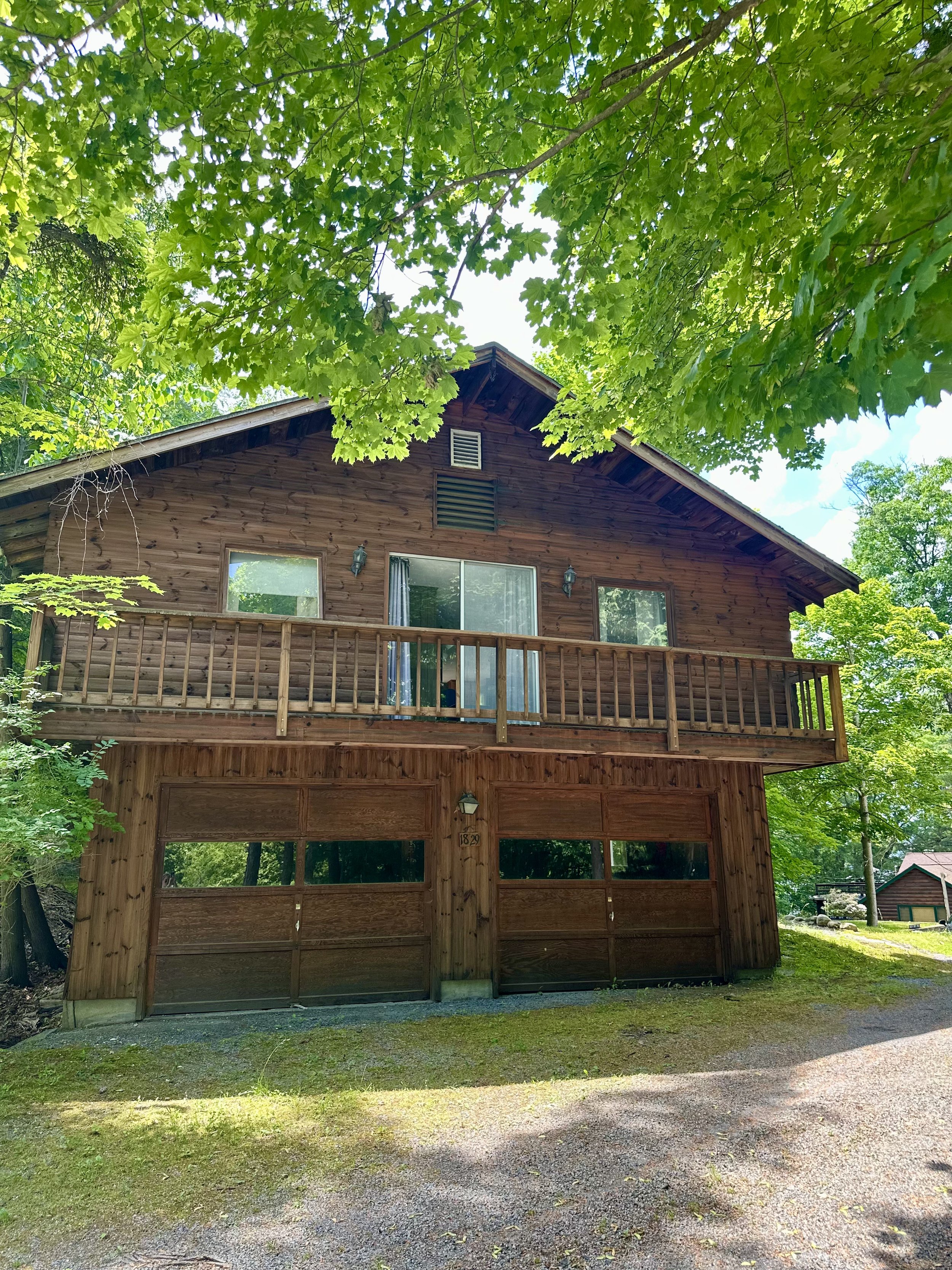 A wooden house with a deck on the second floor, surrounded by green trees.