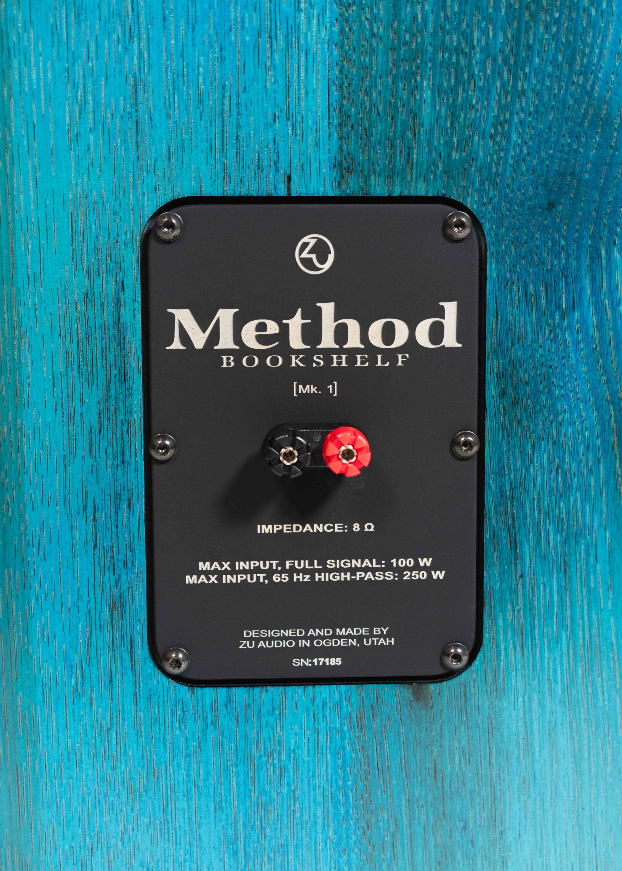 Closeup photo of Zu Method Bookshelf nameplate, finished in tri-coat blue-teal candy over hickory.