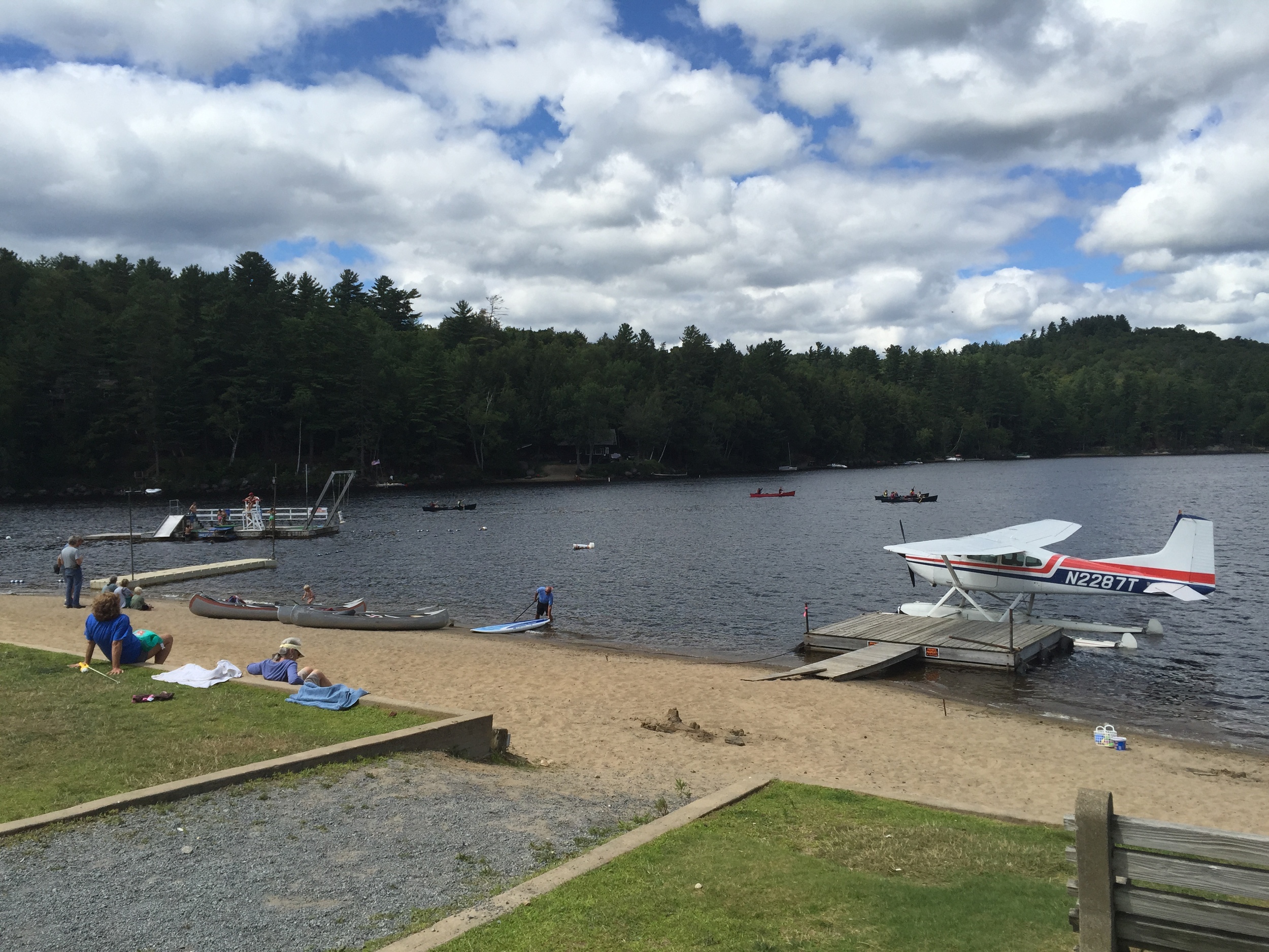 Bi-plane, canoes and town dock on the beach at Long Lake, New York