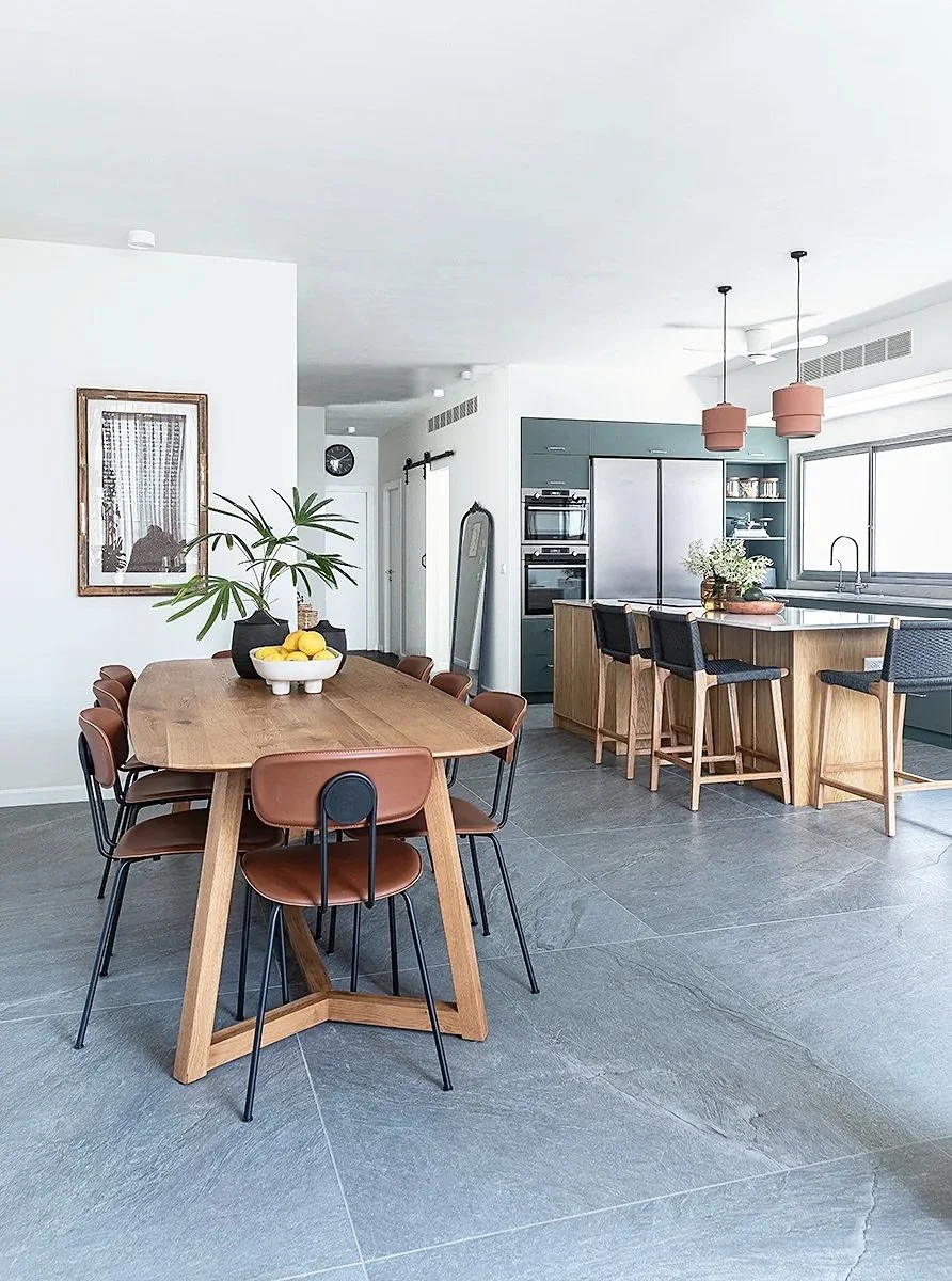 Modern kitchen and dining area with wooden table, black and brown chairs, kitchen island, stainless steel appliances, open window, and minimal decor.      

אדריכלית אירה שריג 