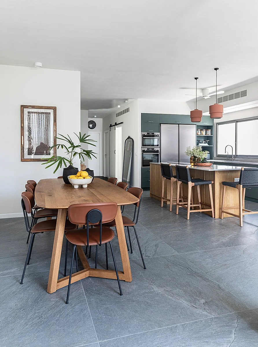 Modern kitchen and dining area with wooden table, black and brown chairs, kitchen island, stainless steel appliances, open window, and minimal decor.