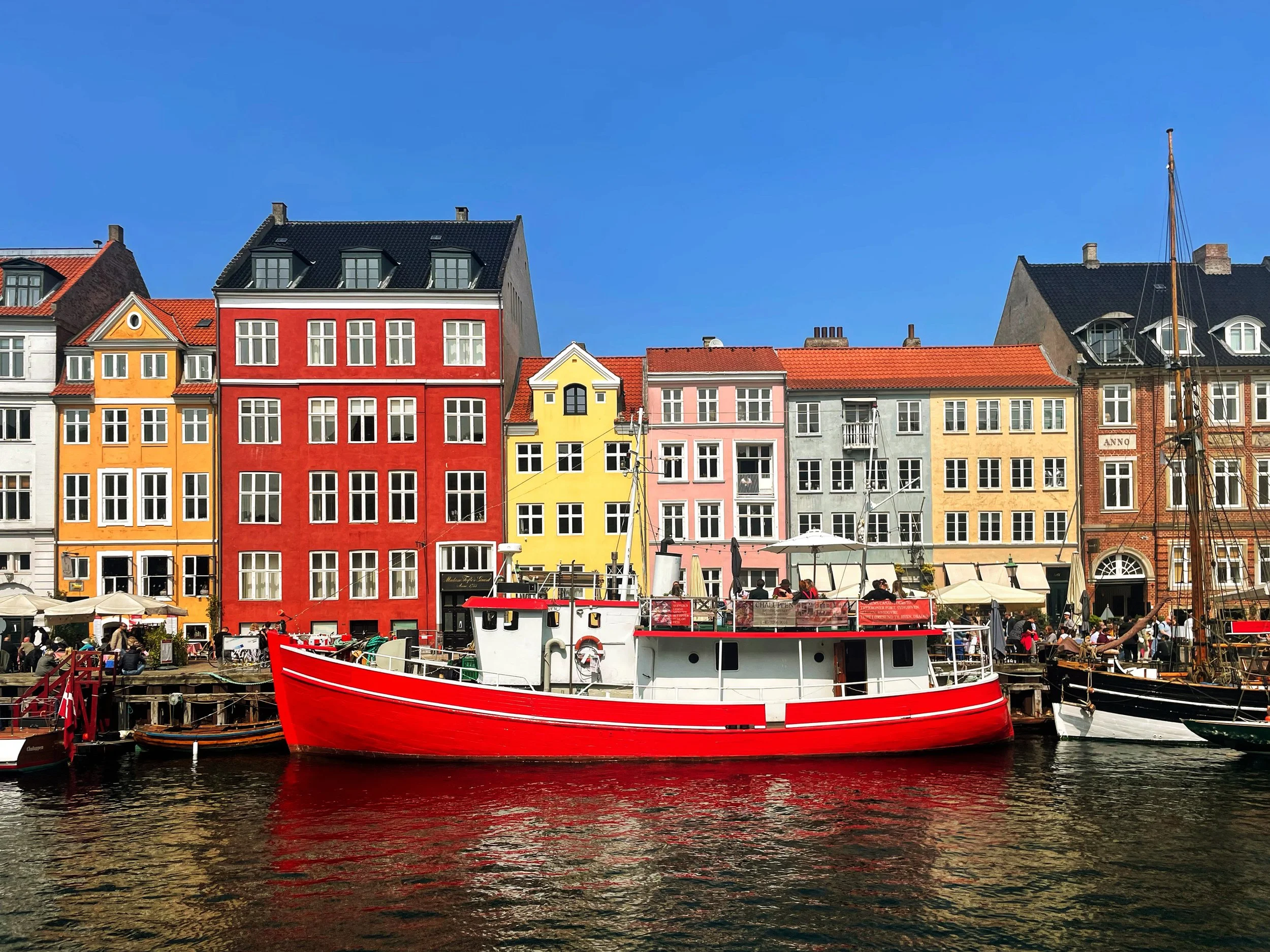 Colorful buildings along a waterfront with boats, including a prominent red and white boat, under a clear blue sky.
