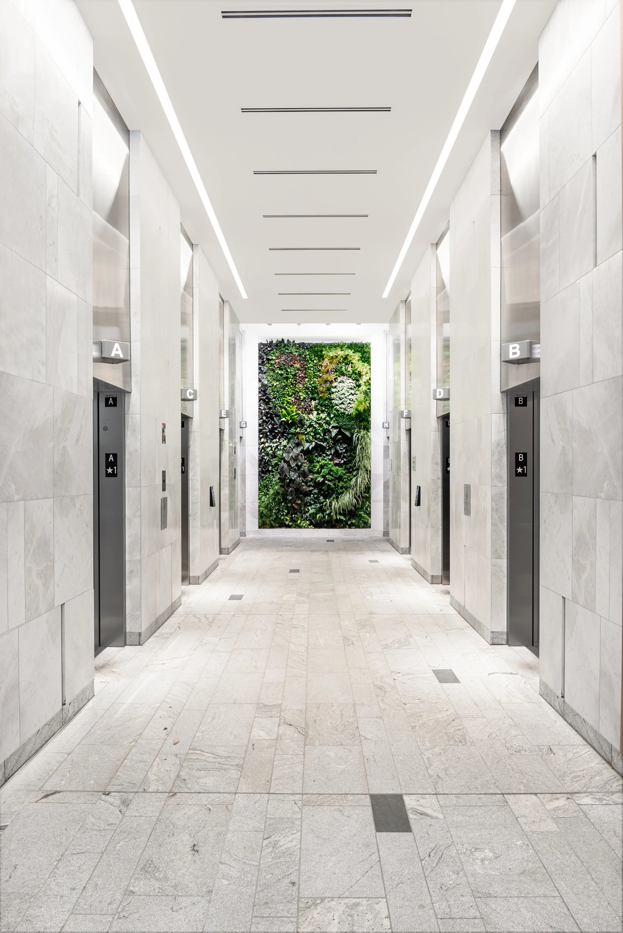 Modern elevator lobby with six elevators on each side, labeled A through F, with a large green wall at the end.