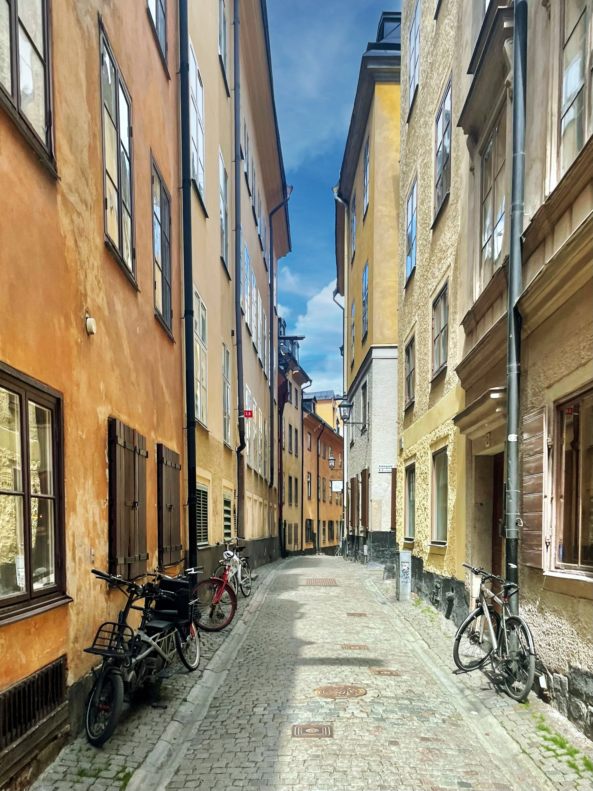 A narrow cobblestone street lined with colorful old buildings on a sunny day, with bicycles parked along the sidewalk.