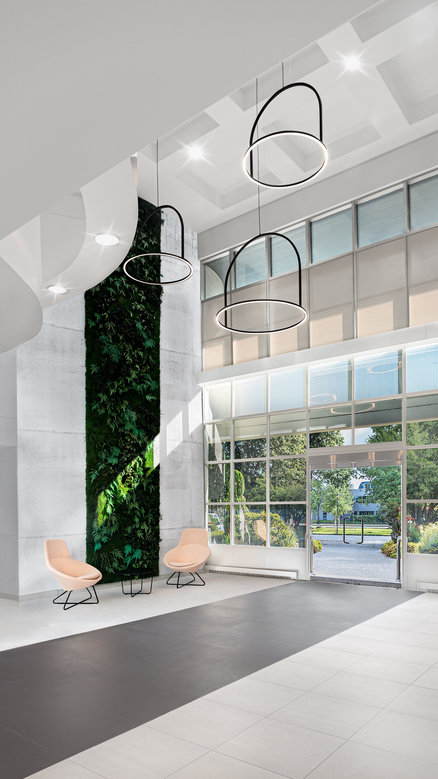 Modern lobby with large glass windows, white walls, two beige chairs, a vertical green plant wall, and contemporary black pendant light fixtures.