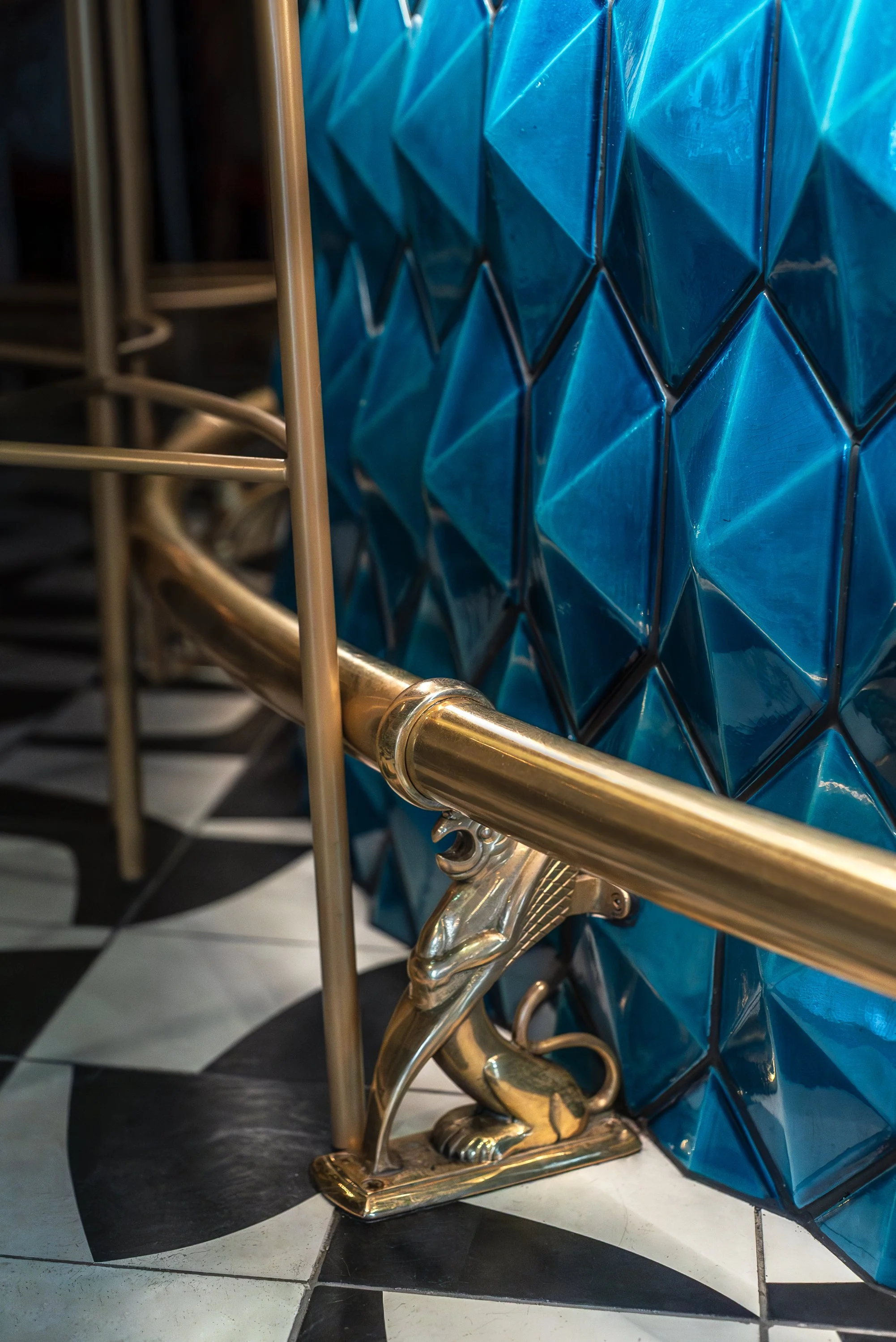 Close-up of a gold lion-shaped sculpture supporting a gold rod, with a blue geometric wall in the background and a black-and-white checkered floor.