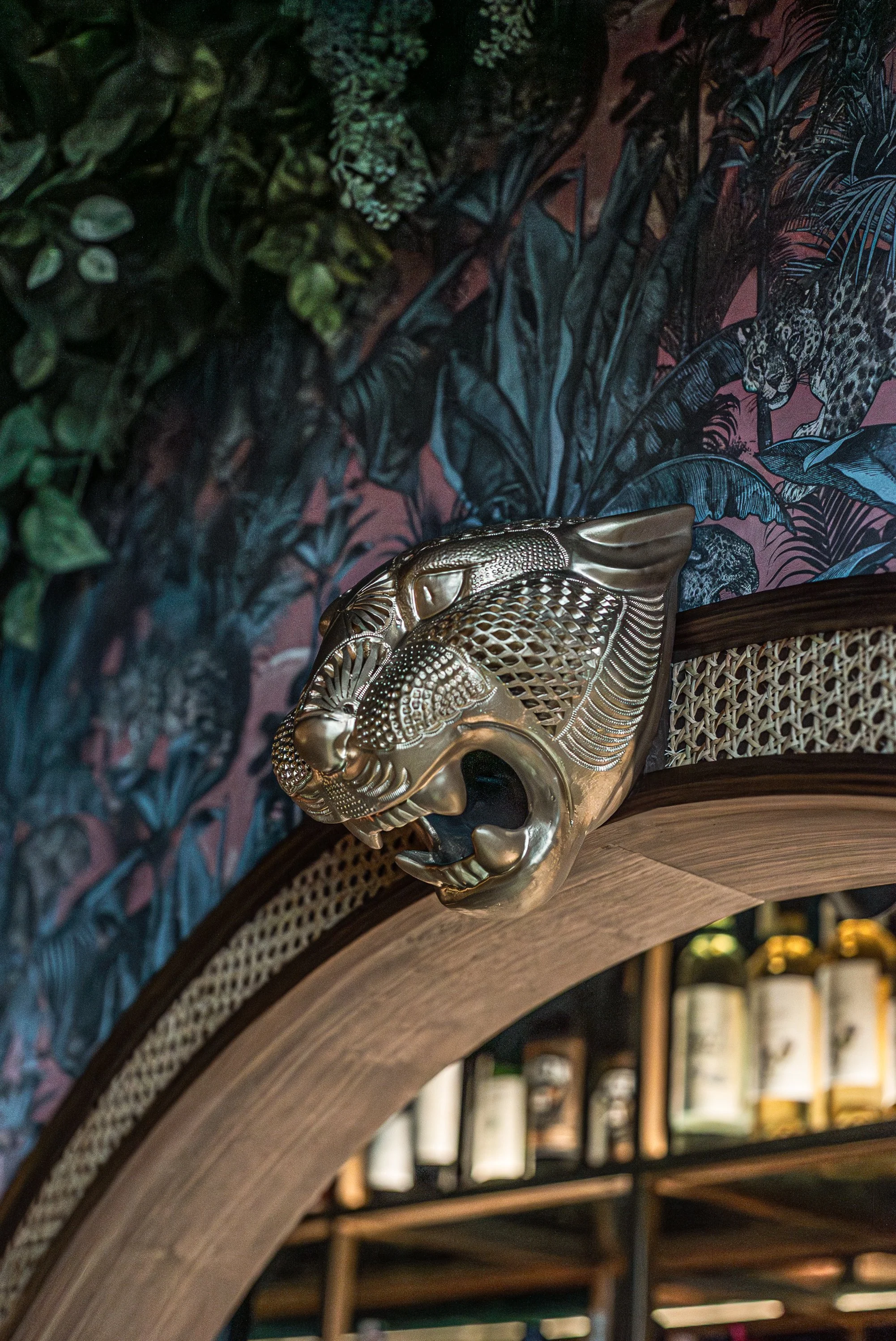 Gold decorative lion head sculpture mounted on a wooden arch with tropical wallpaper background.