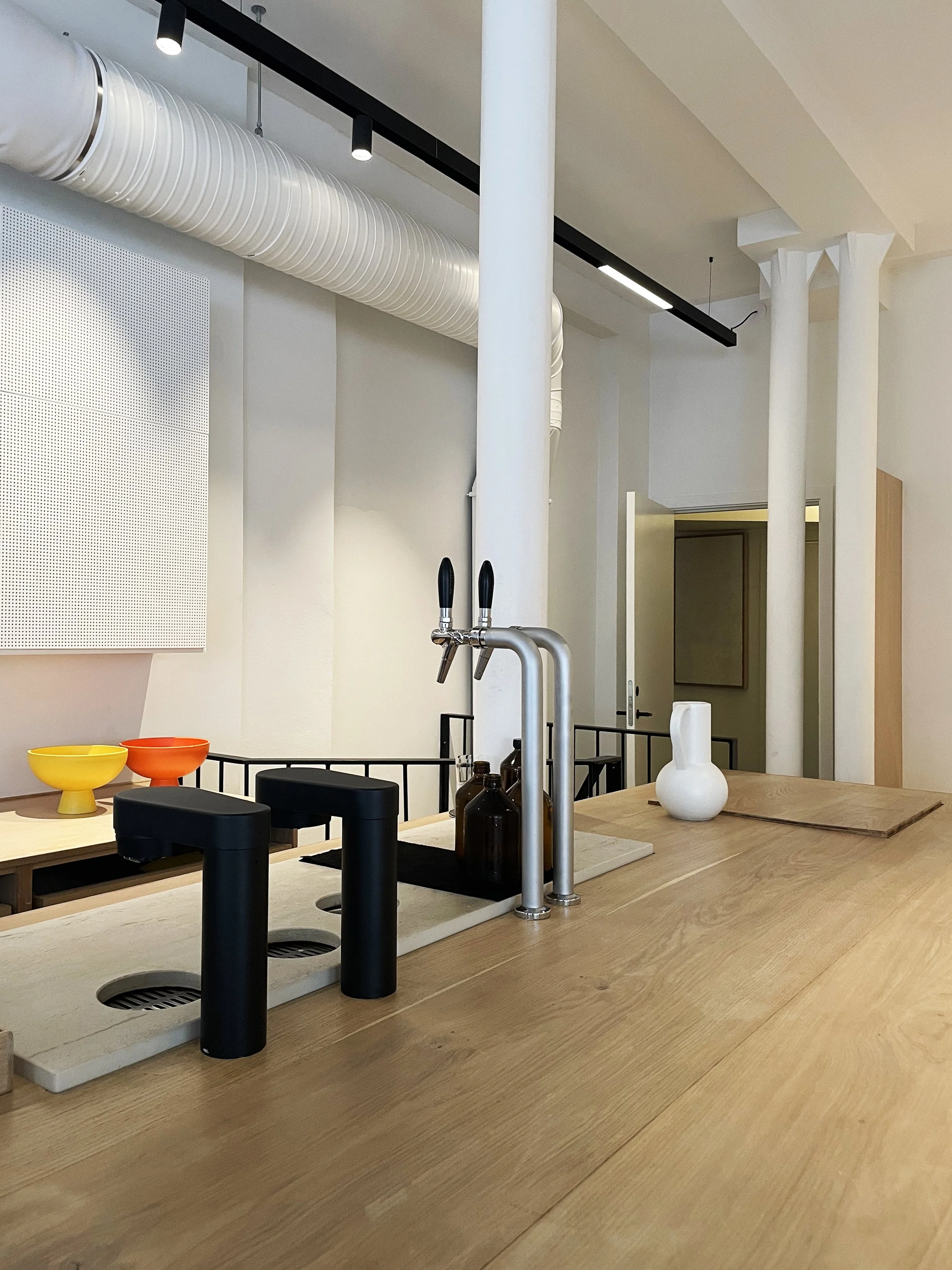Interior view of a minimalist kitchen with a wooden countertop, two black faucets, and decorative bowls and vases.