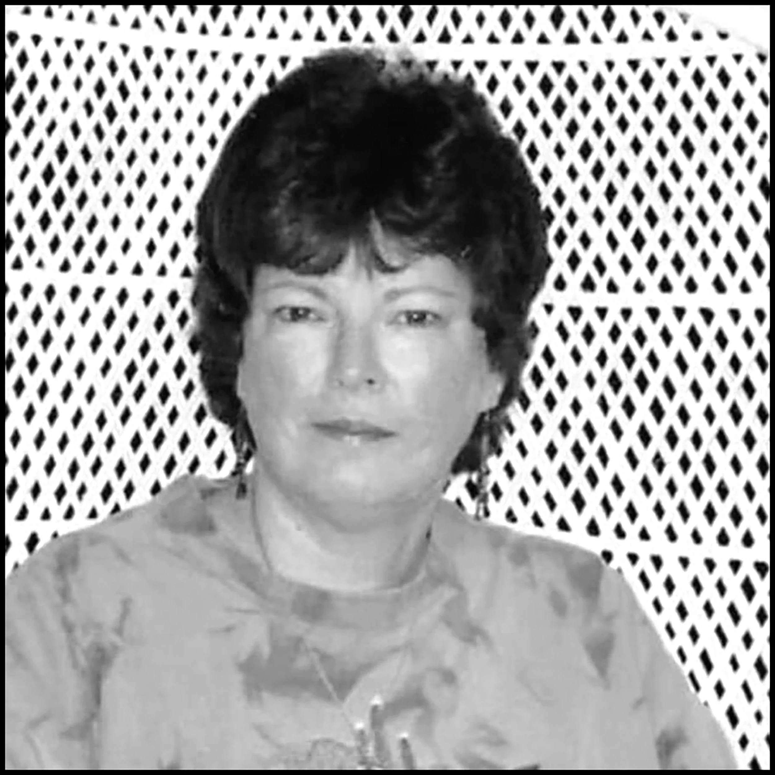 Black and white portrait of a woman with short, curly hair, wearing a patterned blouse, standing in front of a decorative lattice background.